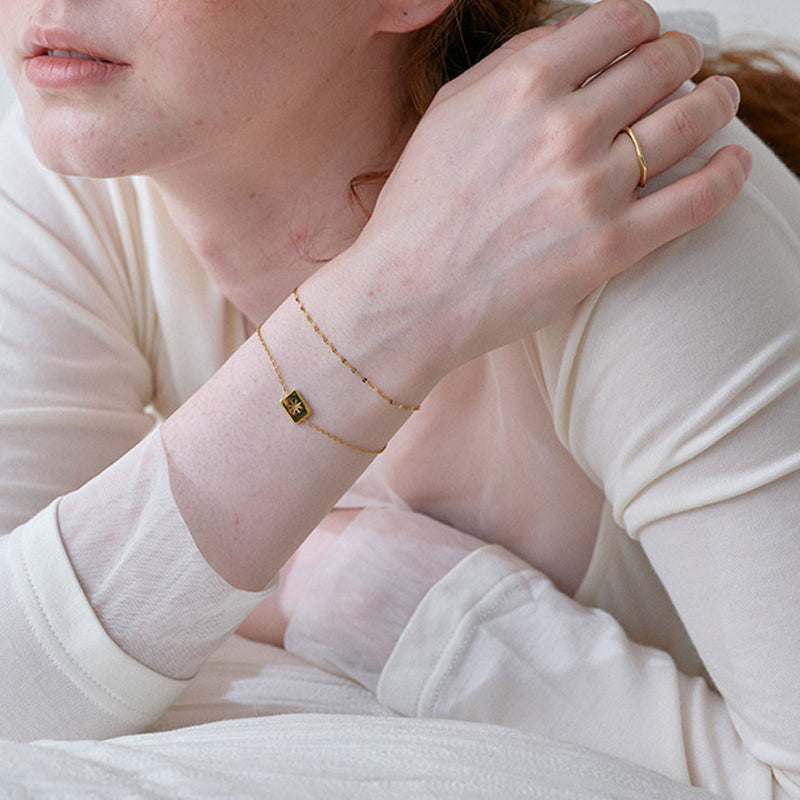 Woman wearing a delicate gold-plated bracelet with a black square charm and a simple gold ring
