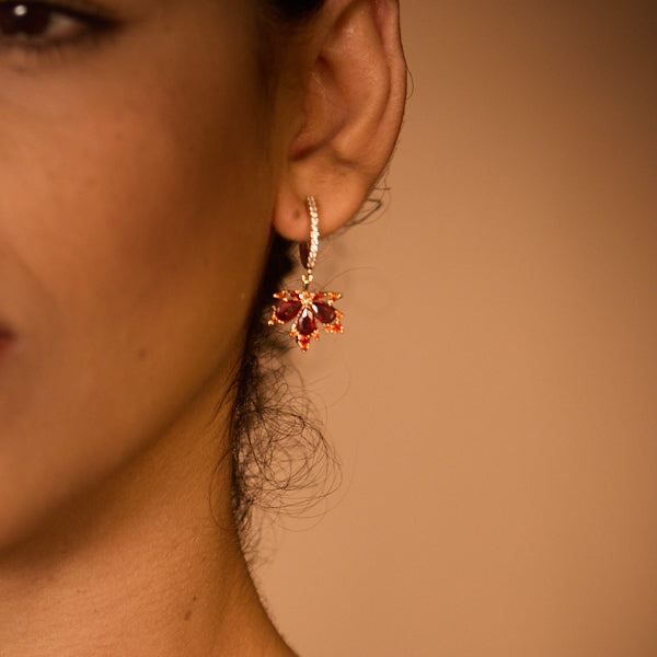Gold-plated hoop earring with red gemstones in floral design on woman's ear
