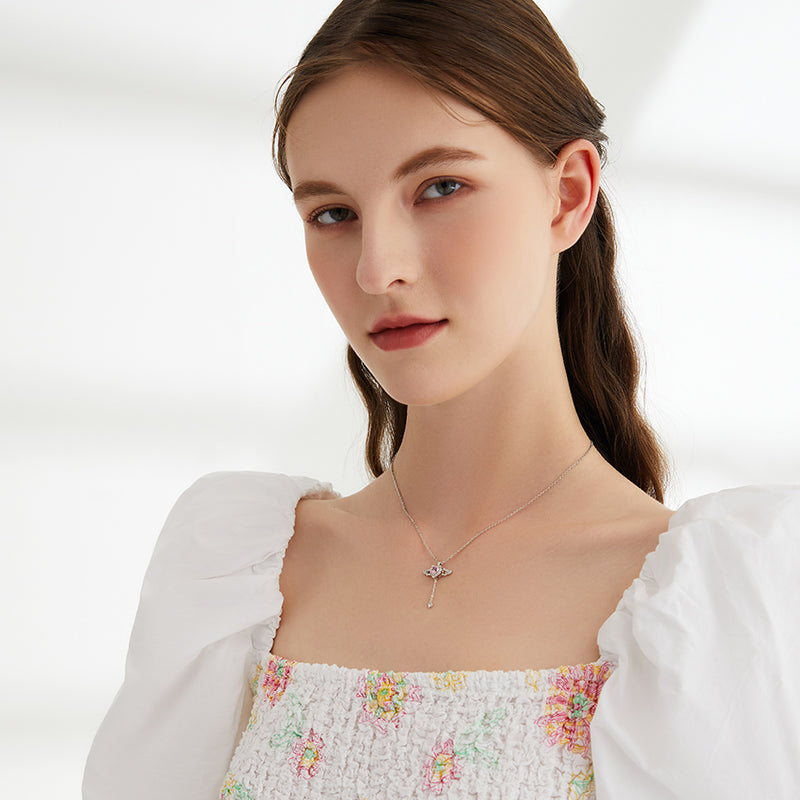 Woman wearing a delicate gold-plated necklace with a pendant, in a white floral dress.