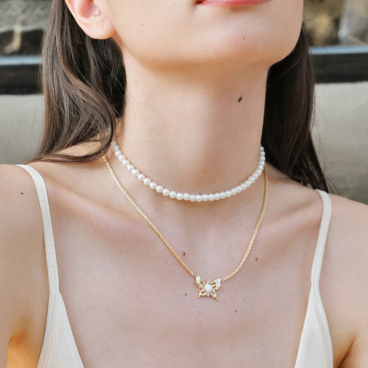 Woman wearing layered pearl choker and gold butterfly pendant necklace