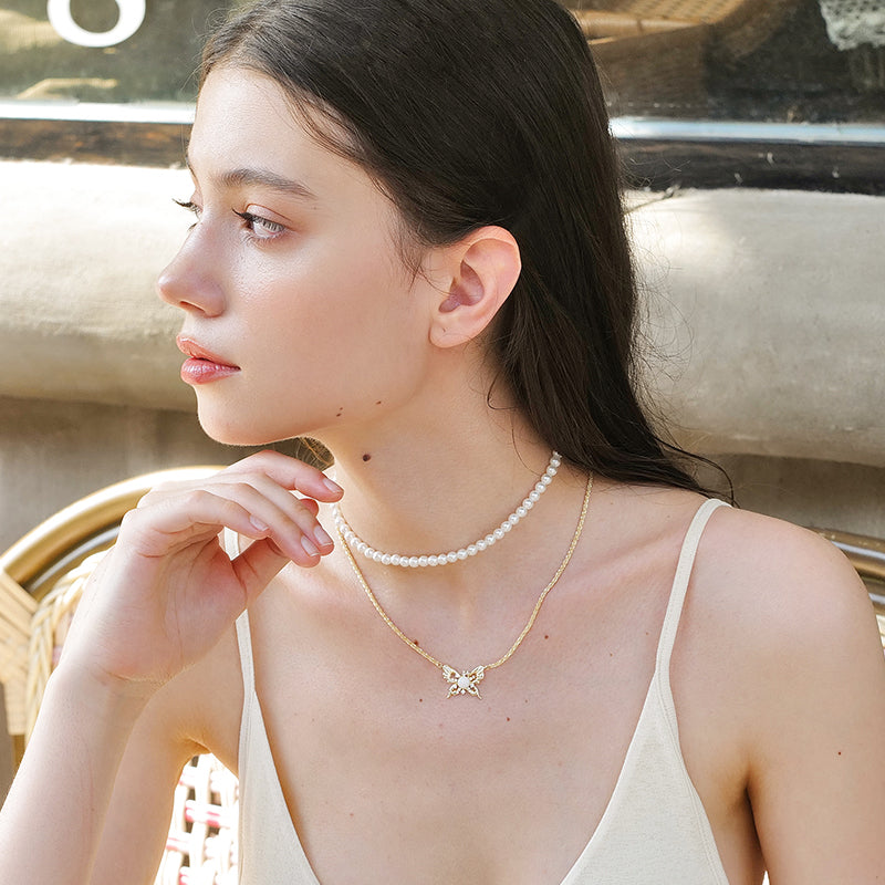 Woman wearing layered pearl choker and gold butterfly pendant necklace outdoors