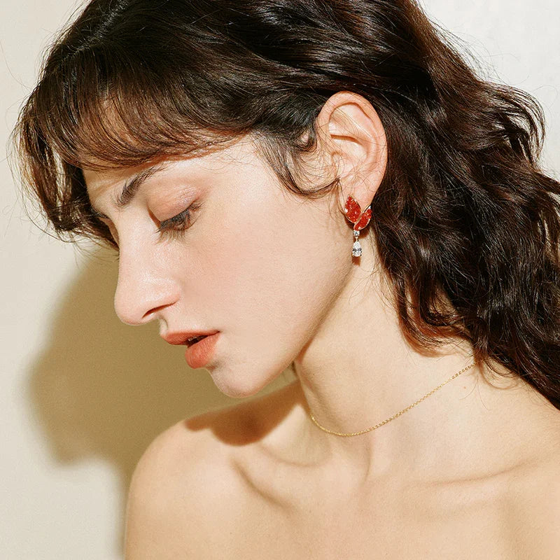 Woman wearing gold-plated minimalist necklace and red statement earrings