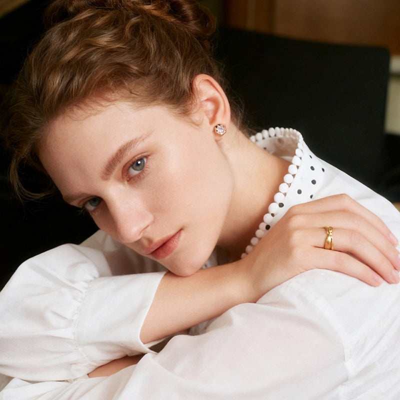 Woman wearing a white blouse with gold-plated ring and crystal stud earrings