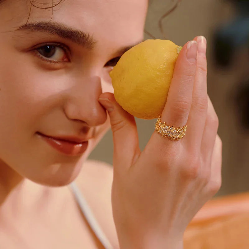 Woman wearing a gold-plated, crystal-embellished ring holding a lemon close to her face