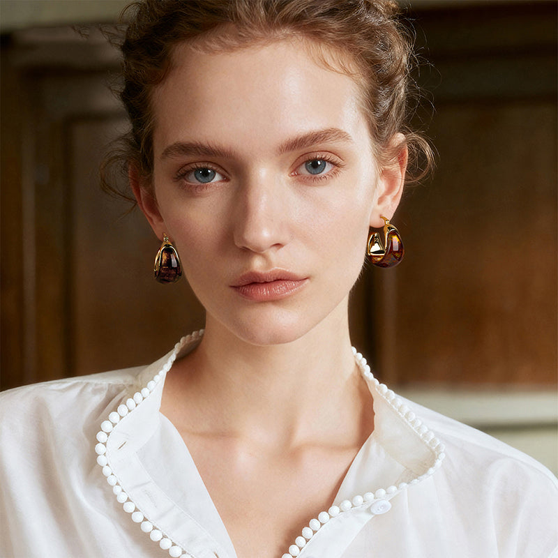 Woman wearing gold-plated statement earrings with marbled accents, white blouse