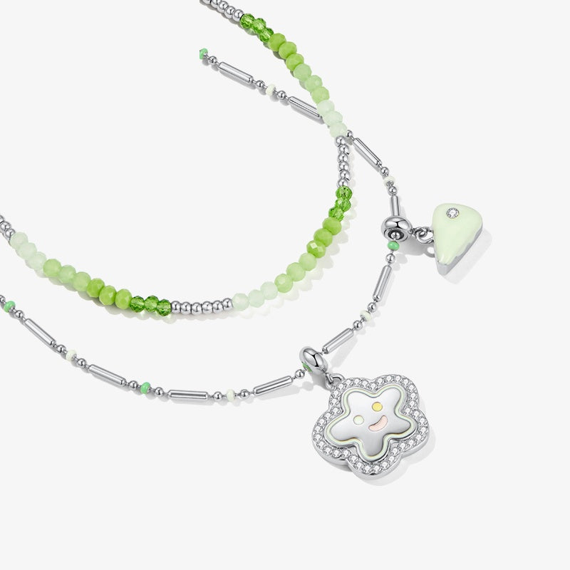Layered green beaded necklace with flower and triangle pendants, silver accents, white background