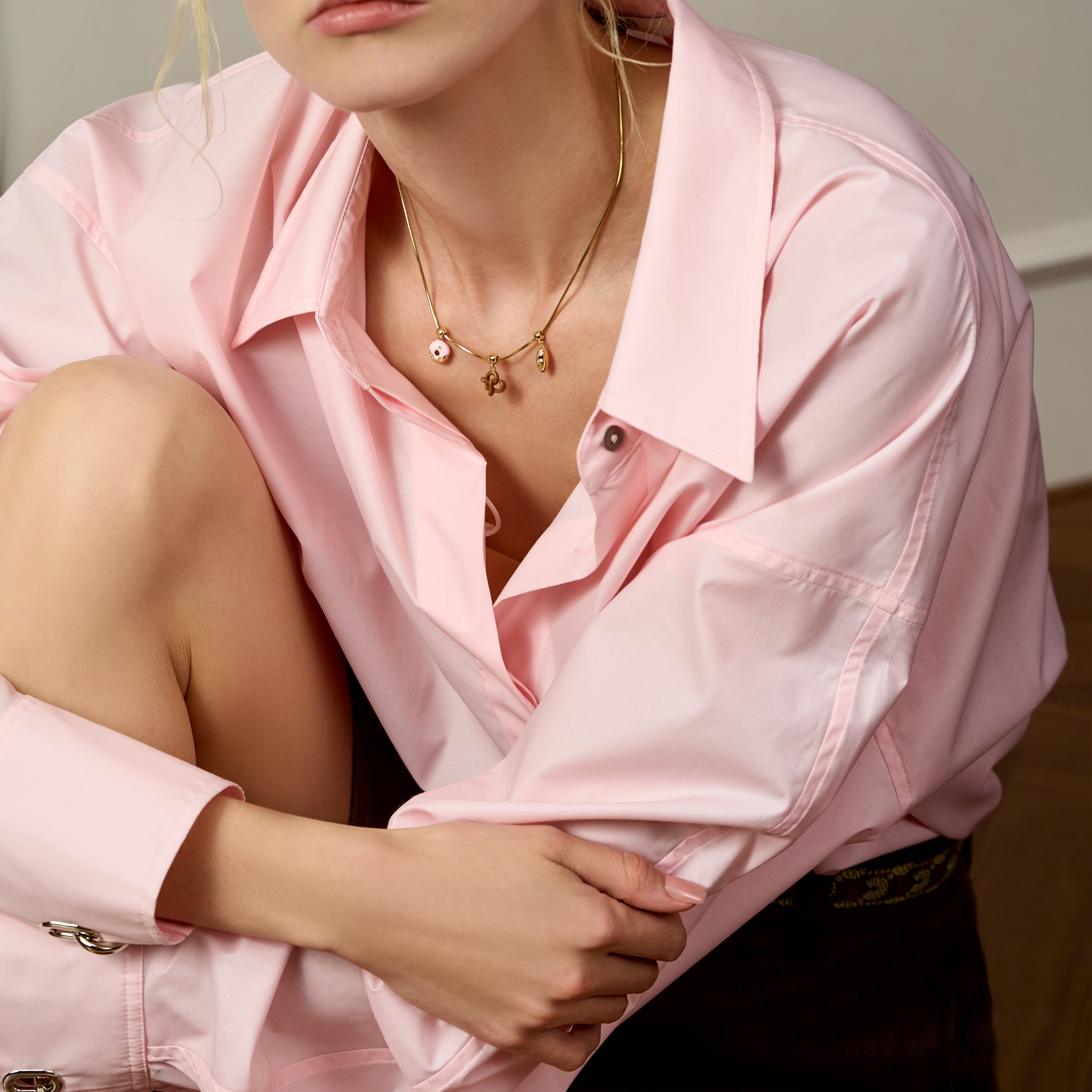 Woman in pink button-down shirt wearing gold-plated charm necklace, elegant jewelry fashion