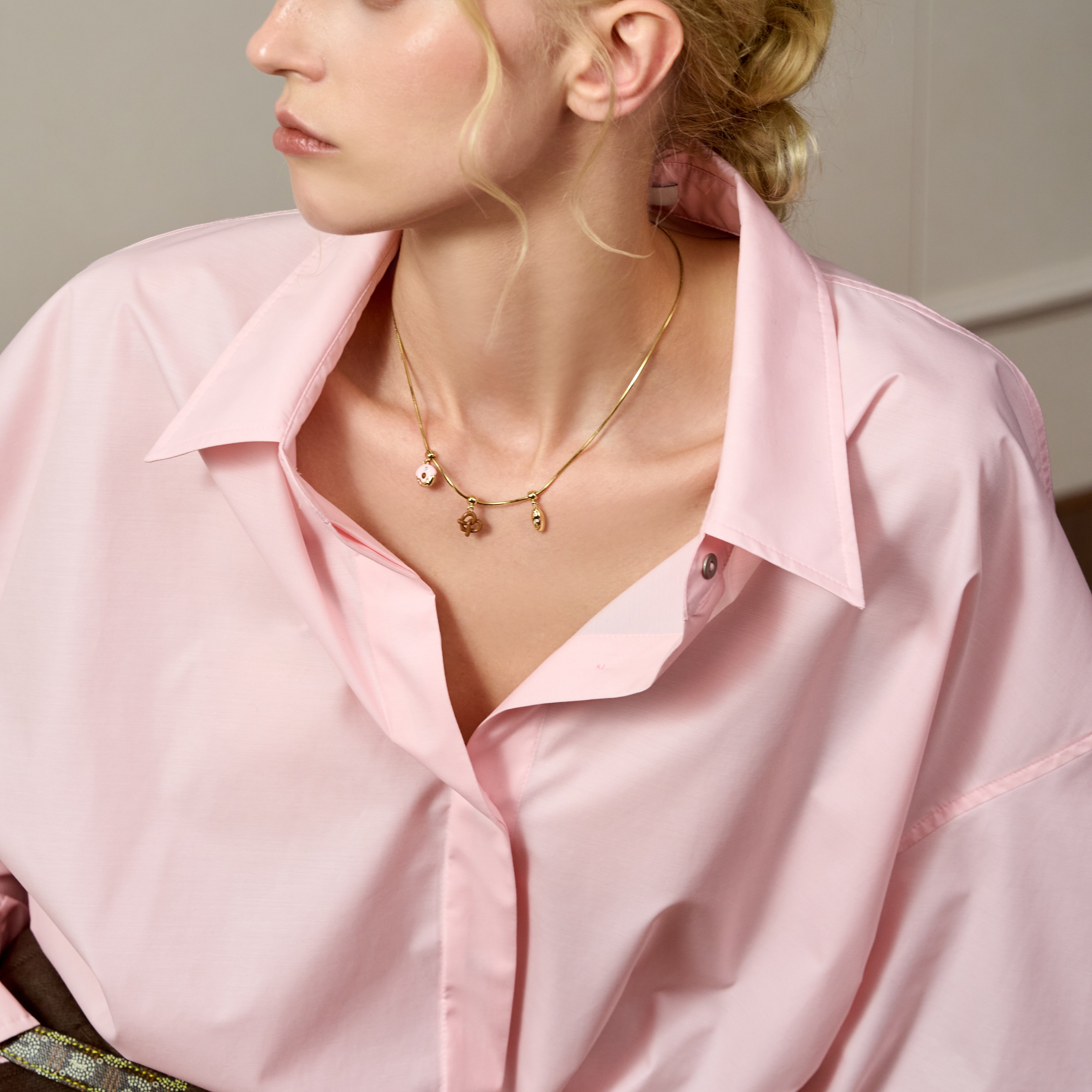 Woman wearing a gold-plated charm necklace and a light pink blouse