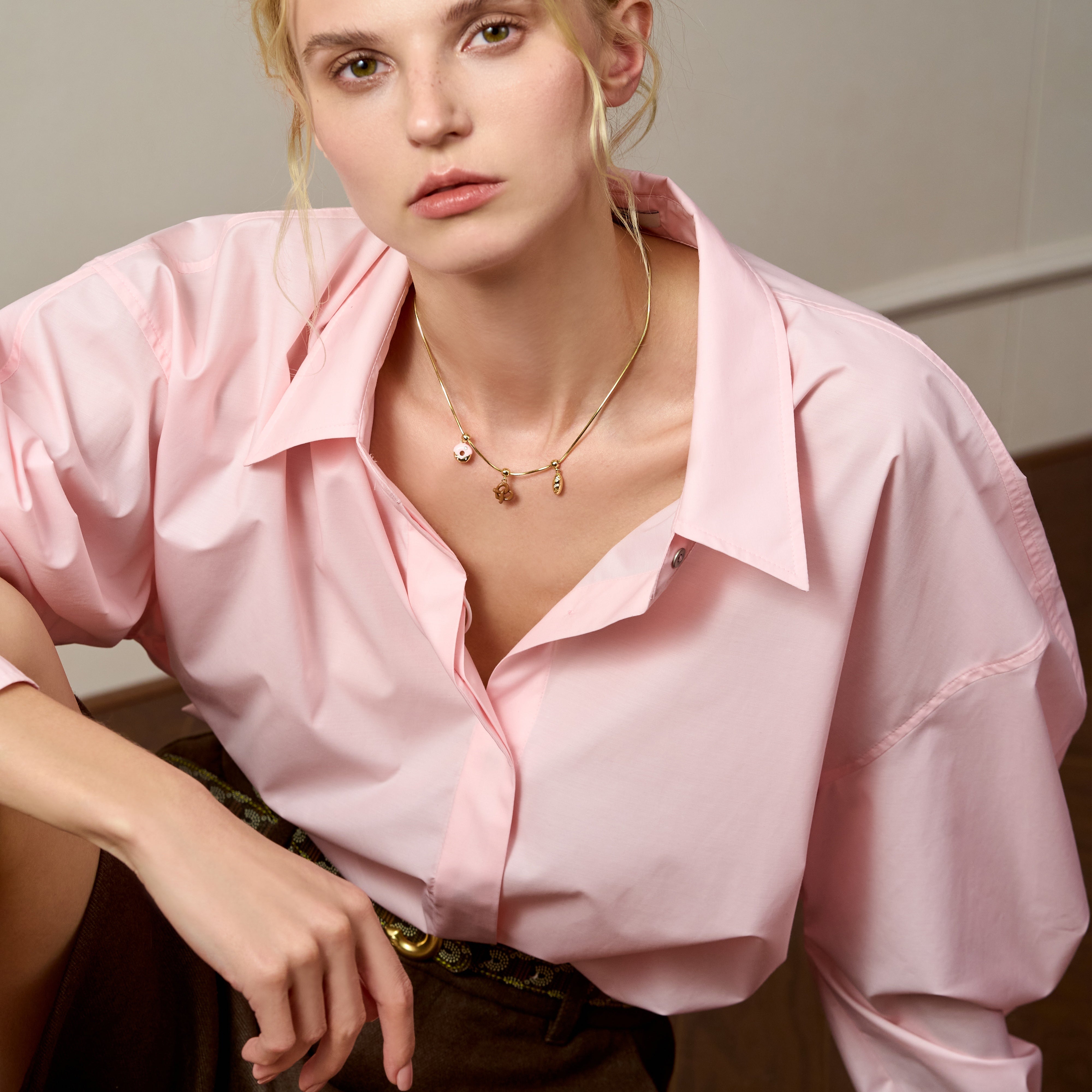 Woman in pink blouse wearing gold-plated charm necklace, statement jewelry fashion