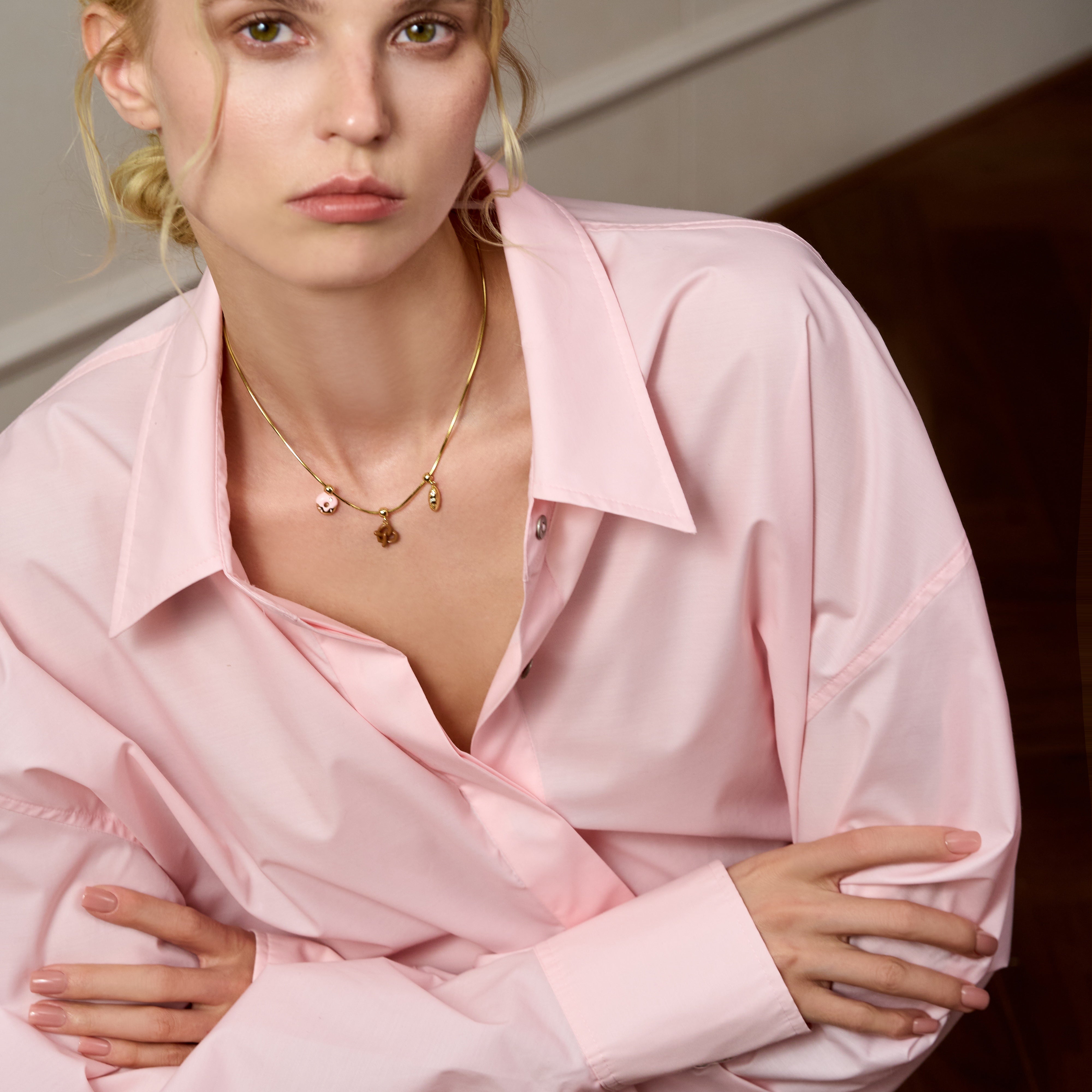 Woman in light pink blouse wearing a gold-plated charm necklace, elegant and stylish look