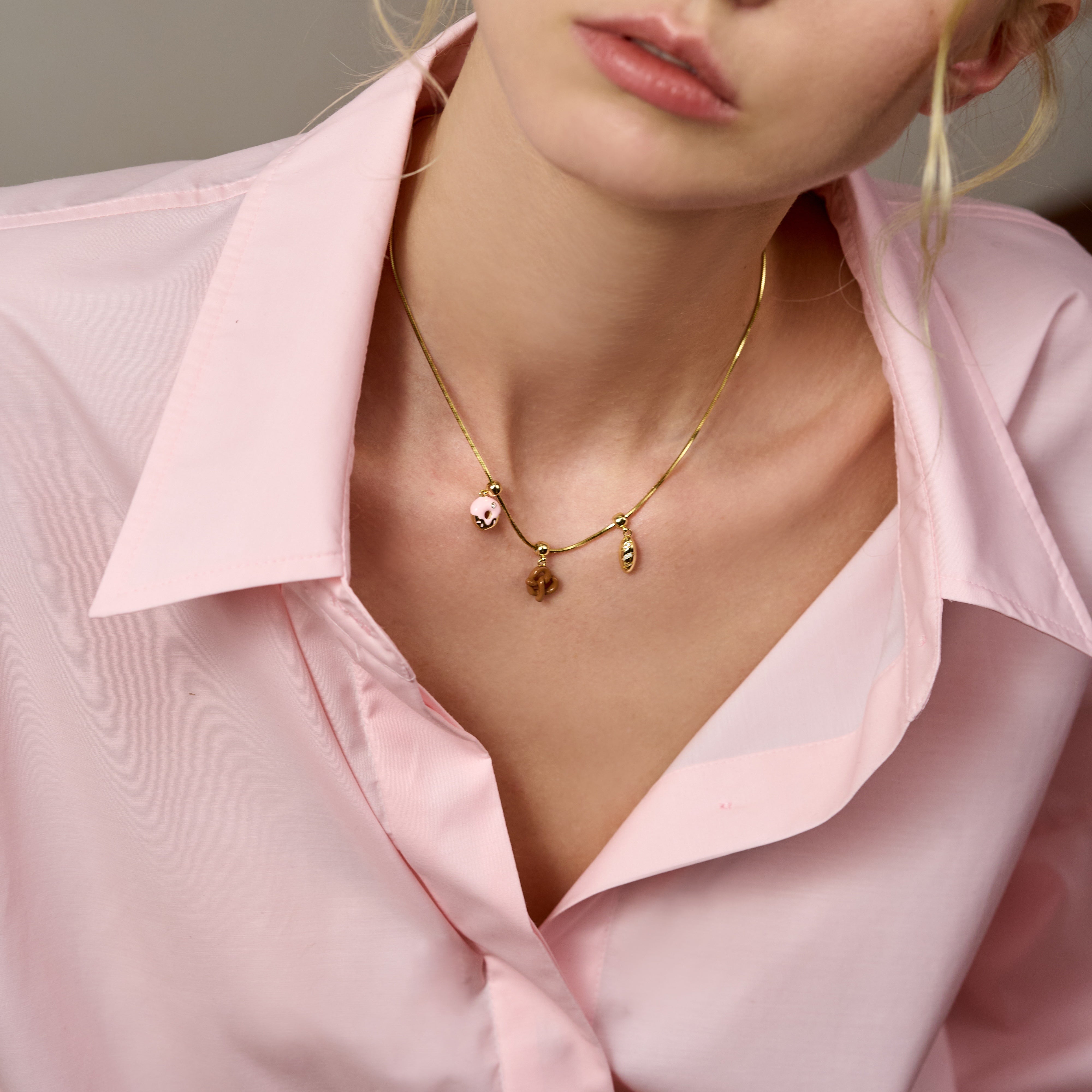 Woman in light pink blouse wearing a gold-plated necklace with three dainty charms
