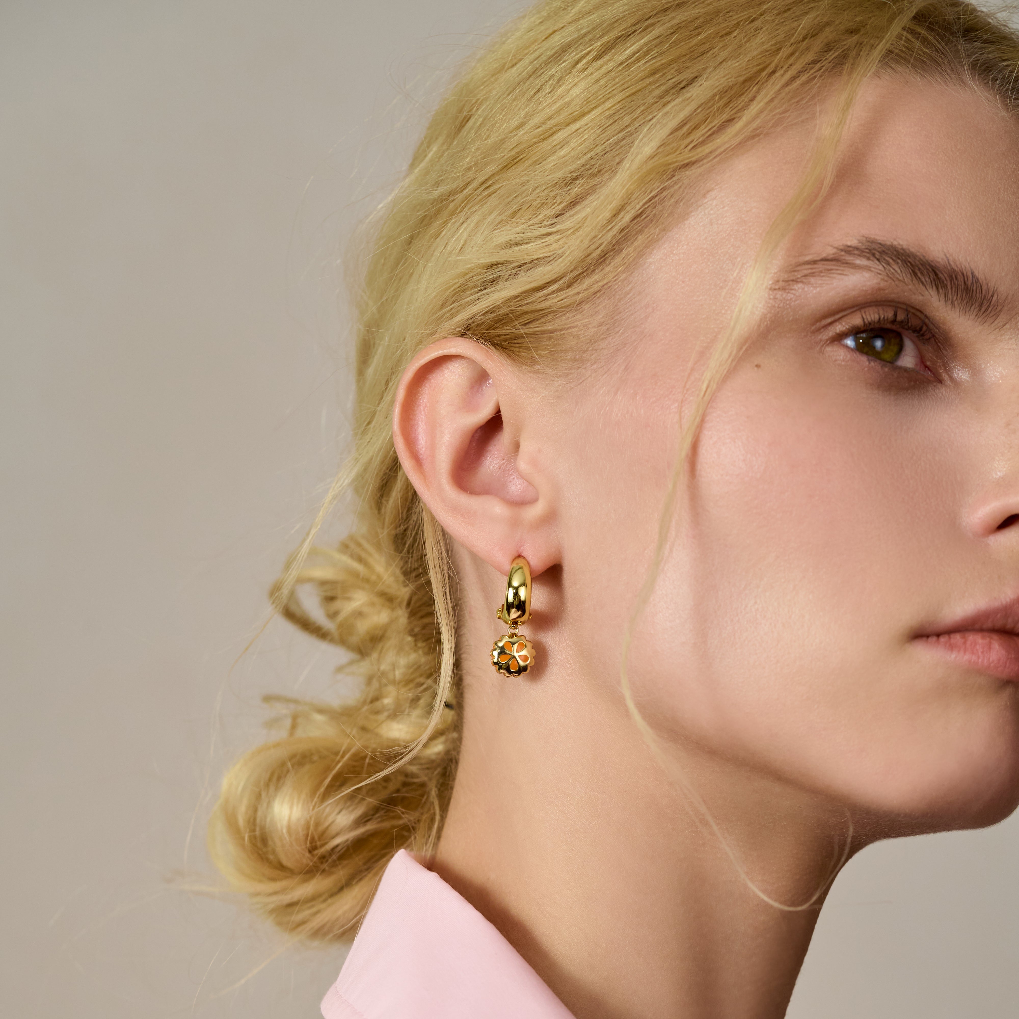 Woman wearing gold-plated hoop earring with flower charm, elegant jewelry close-up