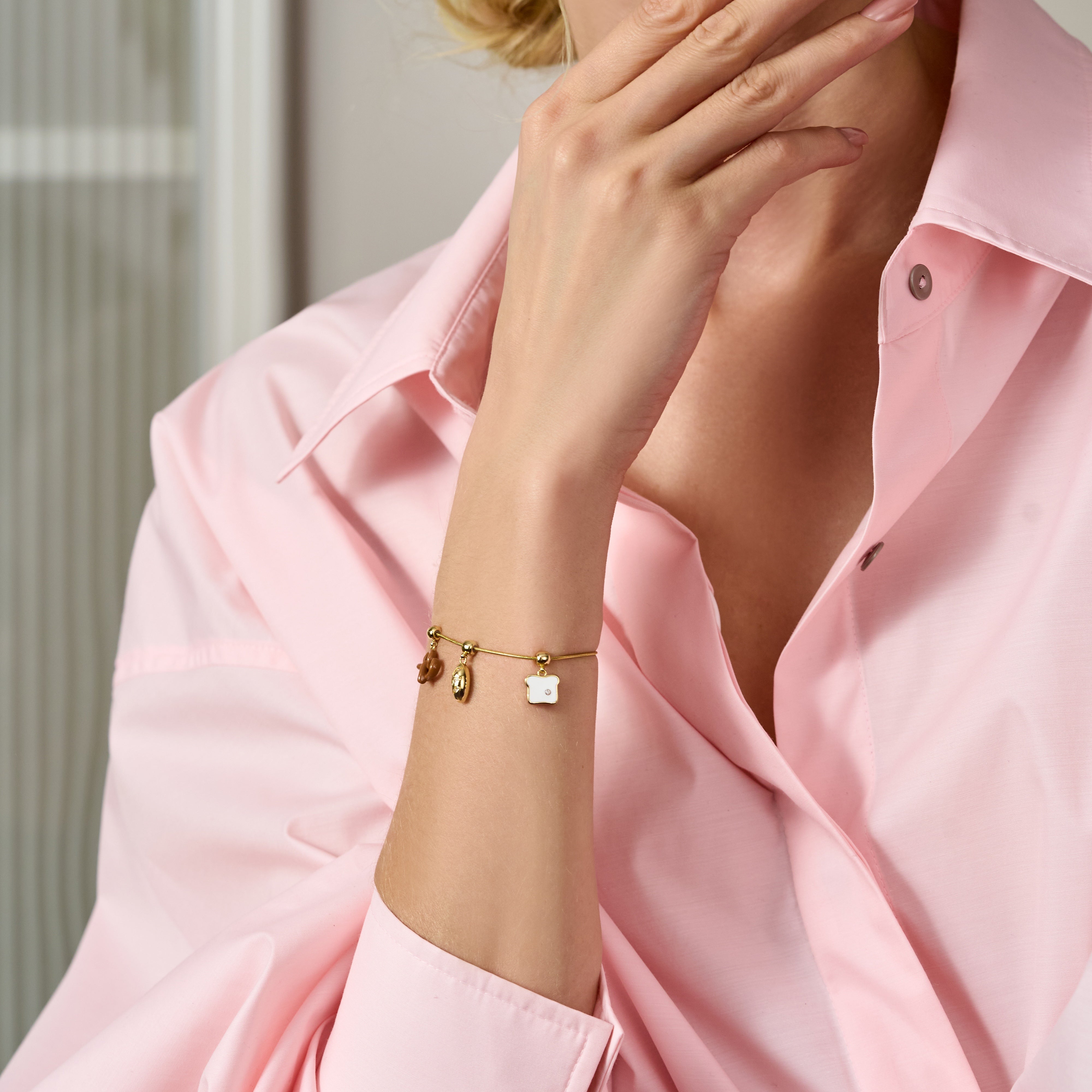 Woman in pink shirt wearing a gold-plated bracelet with three unique charms