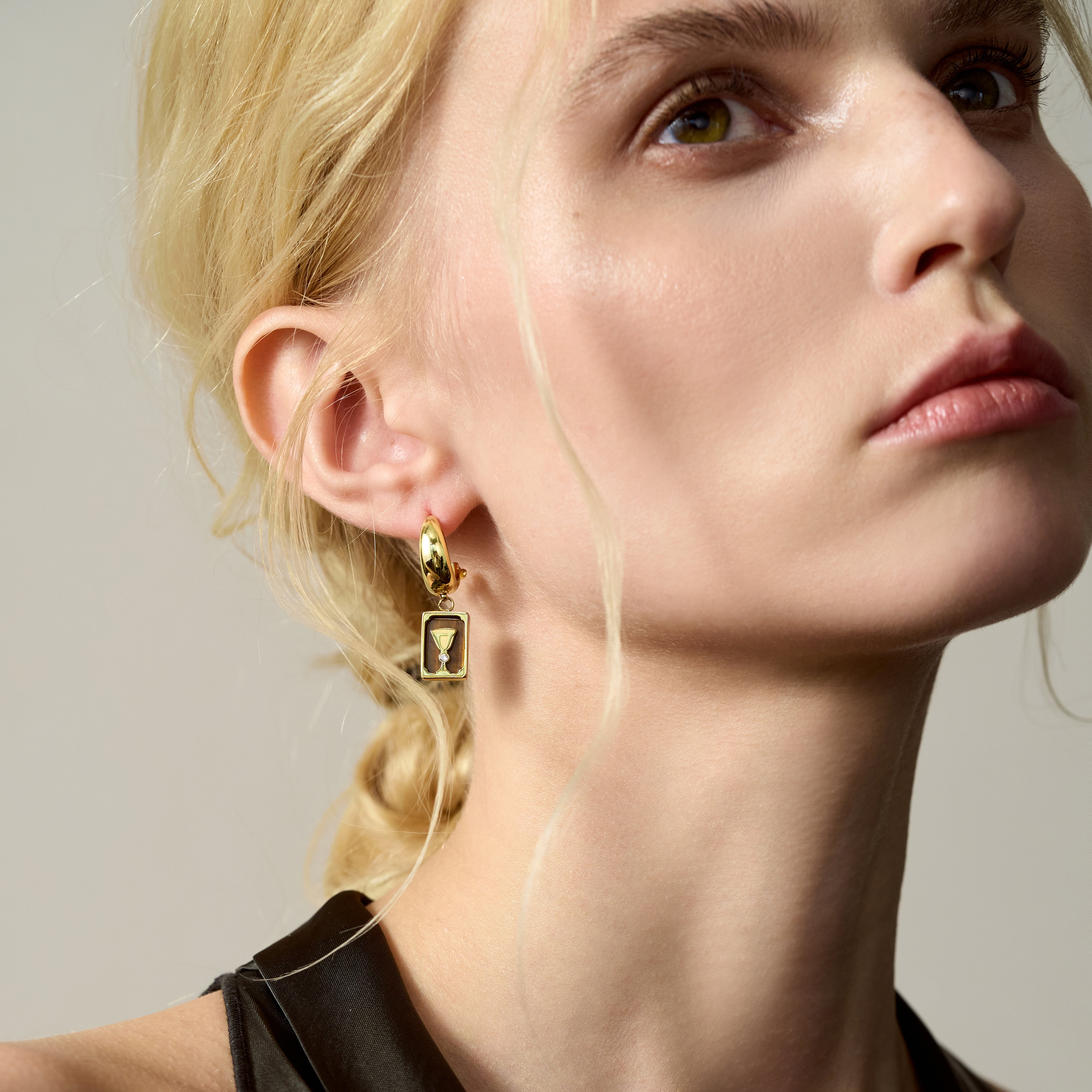 Woman wearing gold-plated statement earring with geometric pendant, close-up portrait