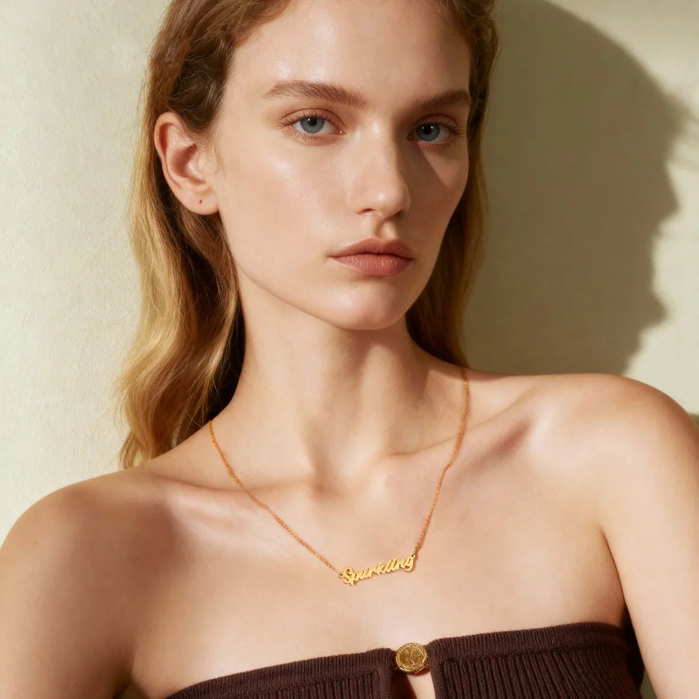 Woman wearing gold-plated 'Sparkling' necklace and brown strapless top, minimal background