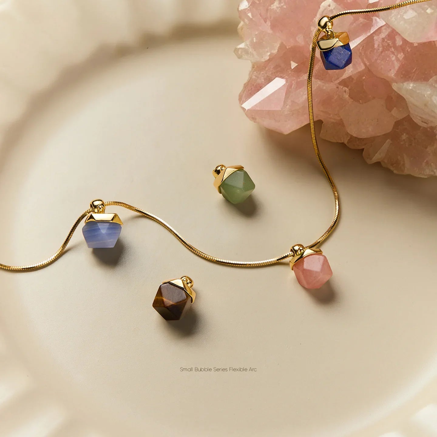 Gold-plated necklace and colorful gemstone pendants on a cream plate by pink crystal
