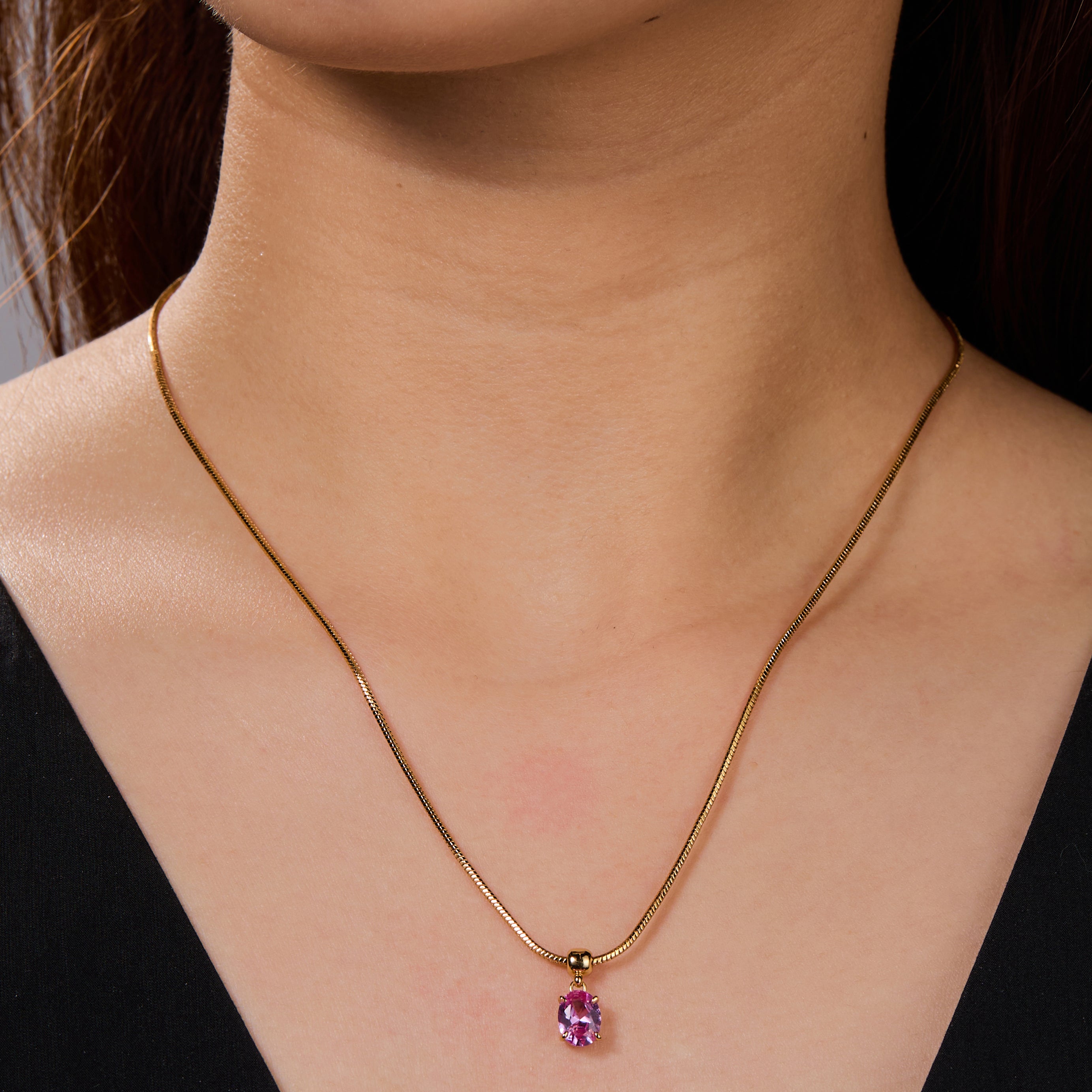 Gold-plated necklace with pink gemstone pendant on woman's neck, elegant jewelry style