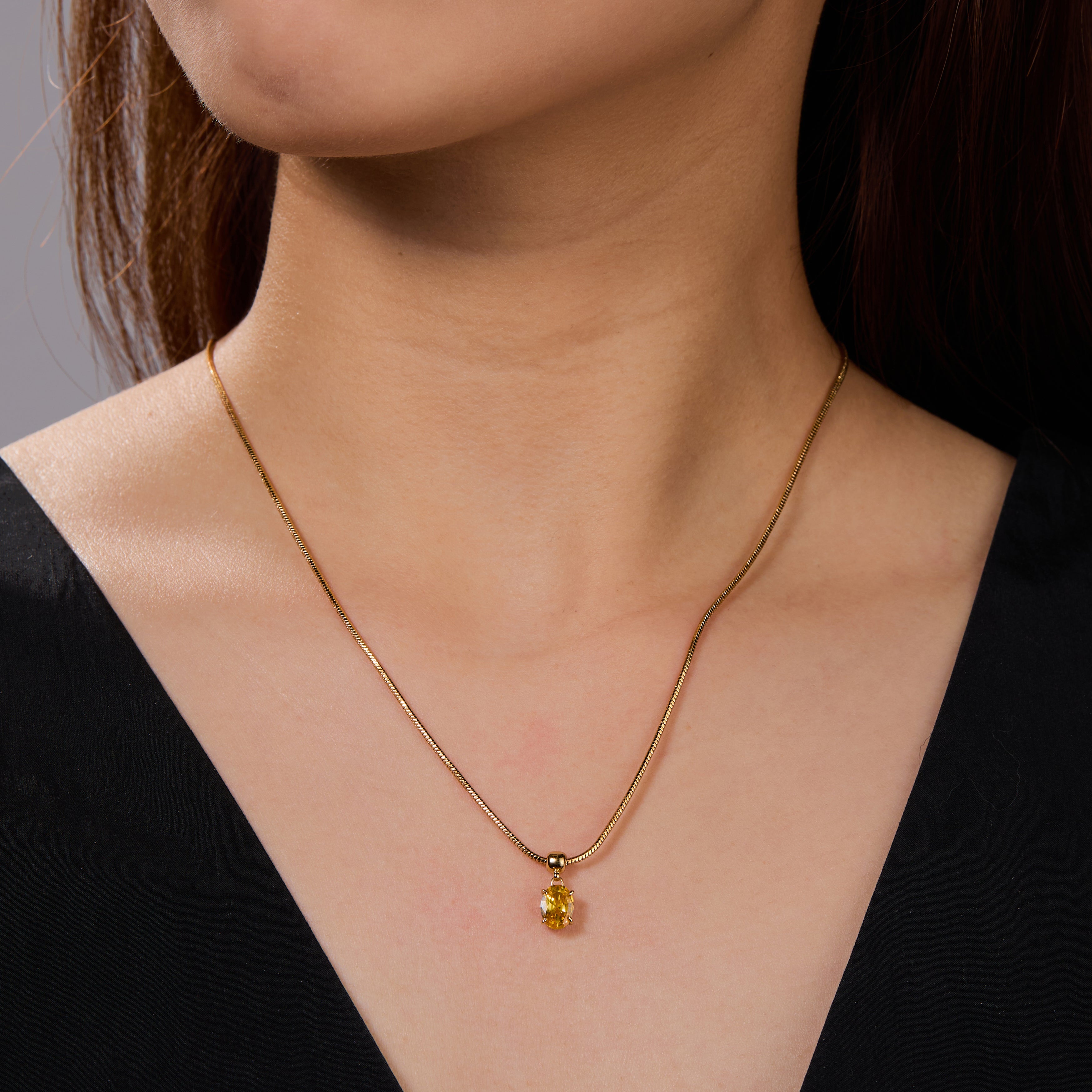 Gold-plated necklace with yellow gemstone pendant on woman wearing black top