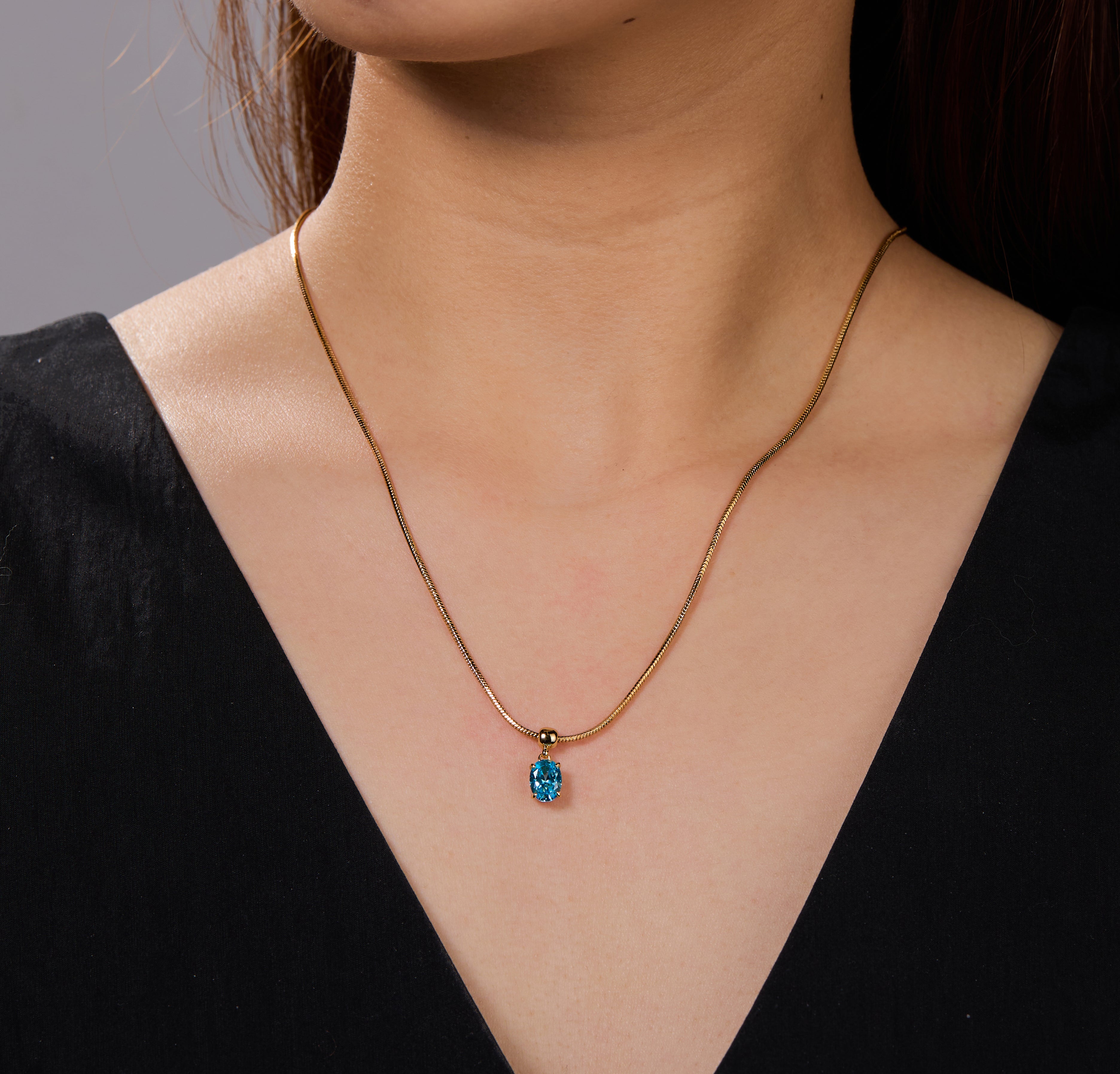 Gold-plated necklace with blue gemstone pendant on woman wearing black v-neck top