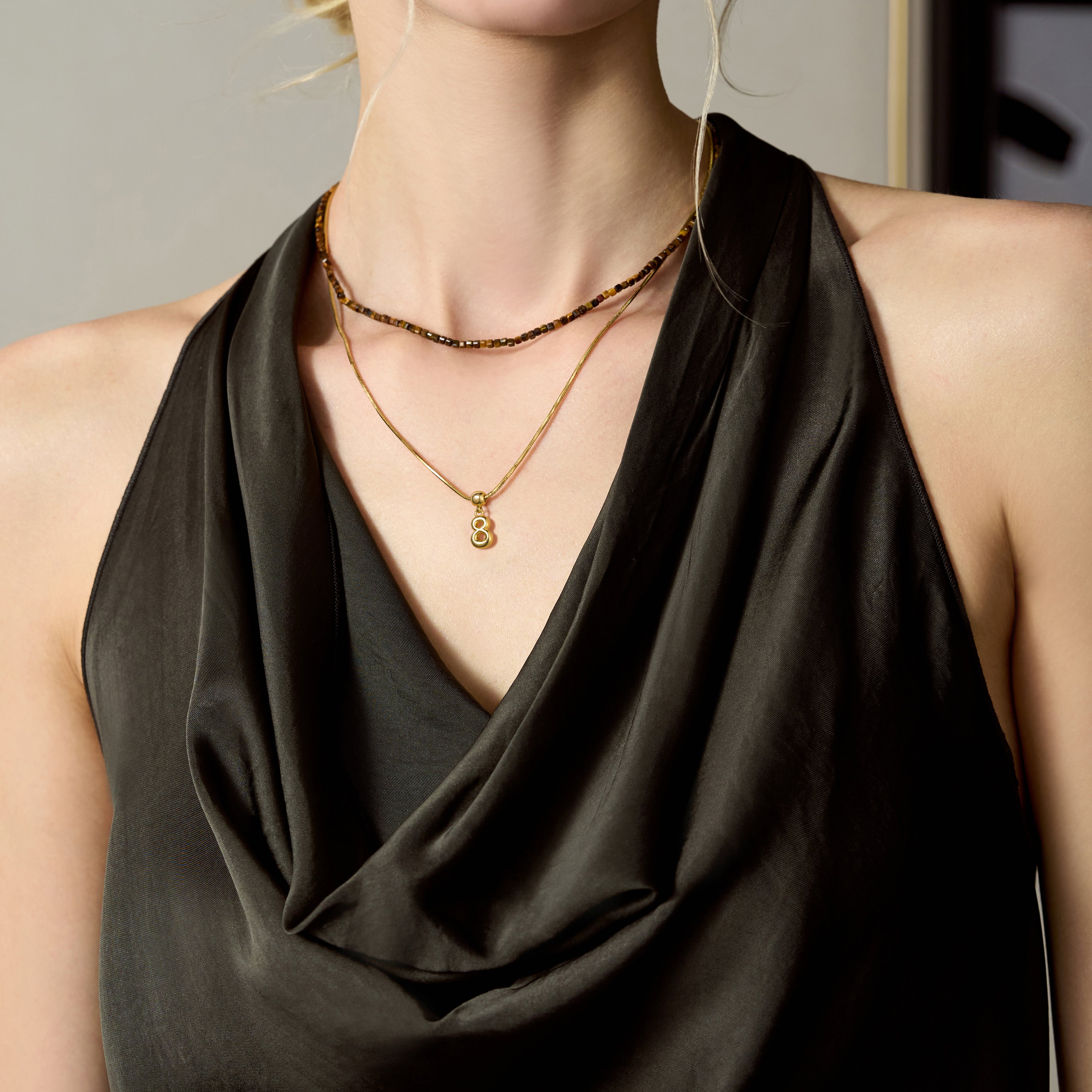 Woman wearing layered gold-plated necklaces with a black satin draped dress