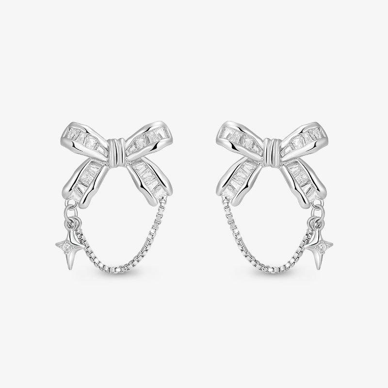 Silver bow-shaped earrings with crystal accents, chain detail, and star charms on white background.
