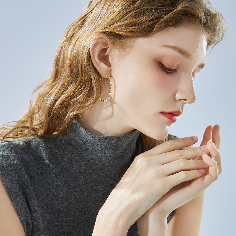Woman wearing large gold-plated hoop earrings and a sleeveless grey turtleneck top