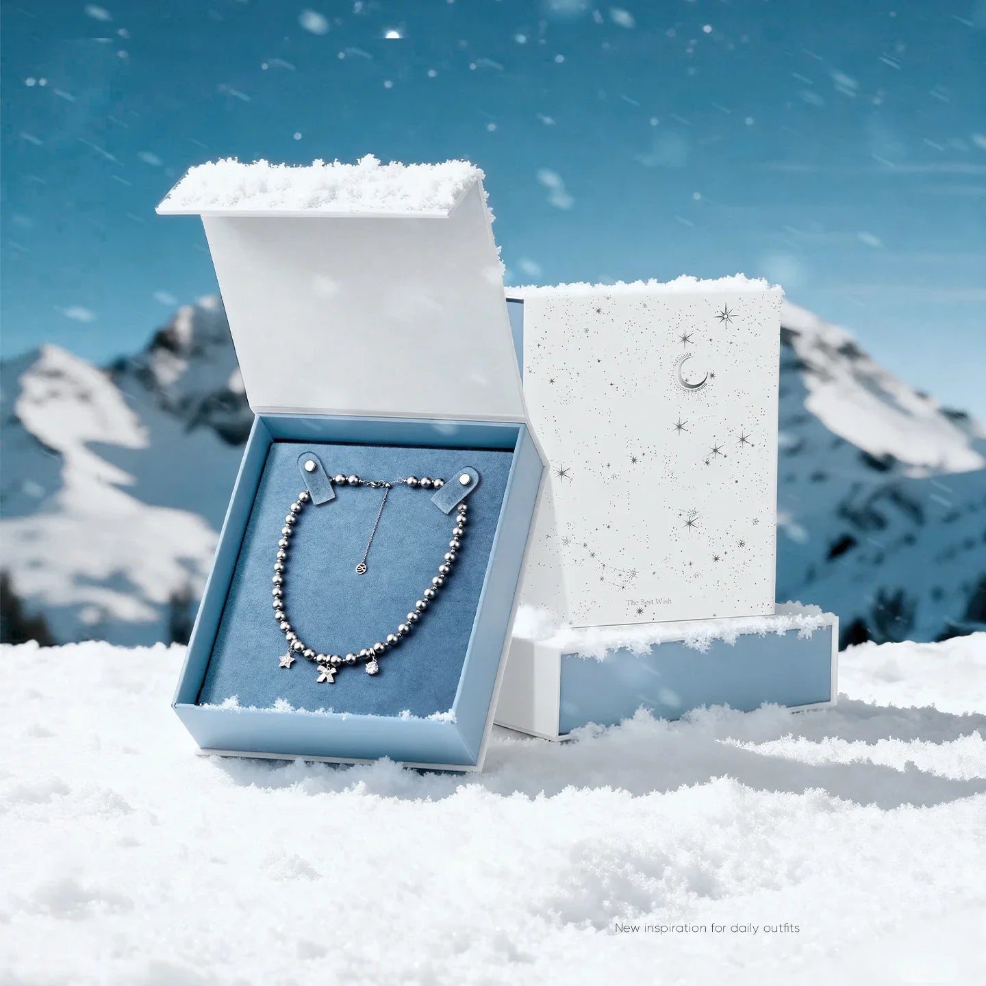 Elegant gold-plated beaded necklace with star charms in a blue jewelry box on snowy mountain.