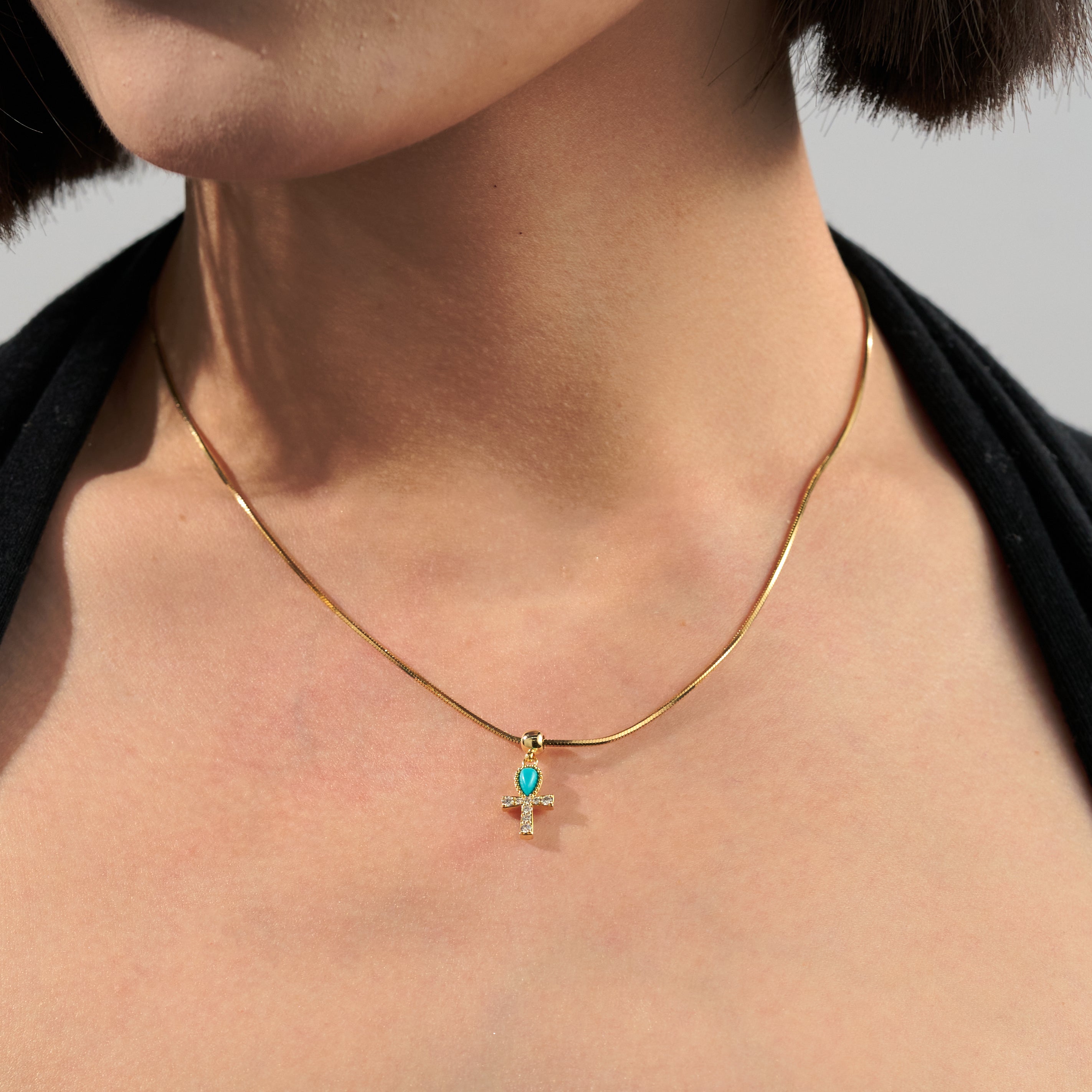 Gold-plated necklace with turquoise and crystal cross pendant on woman's neck