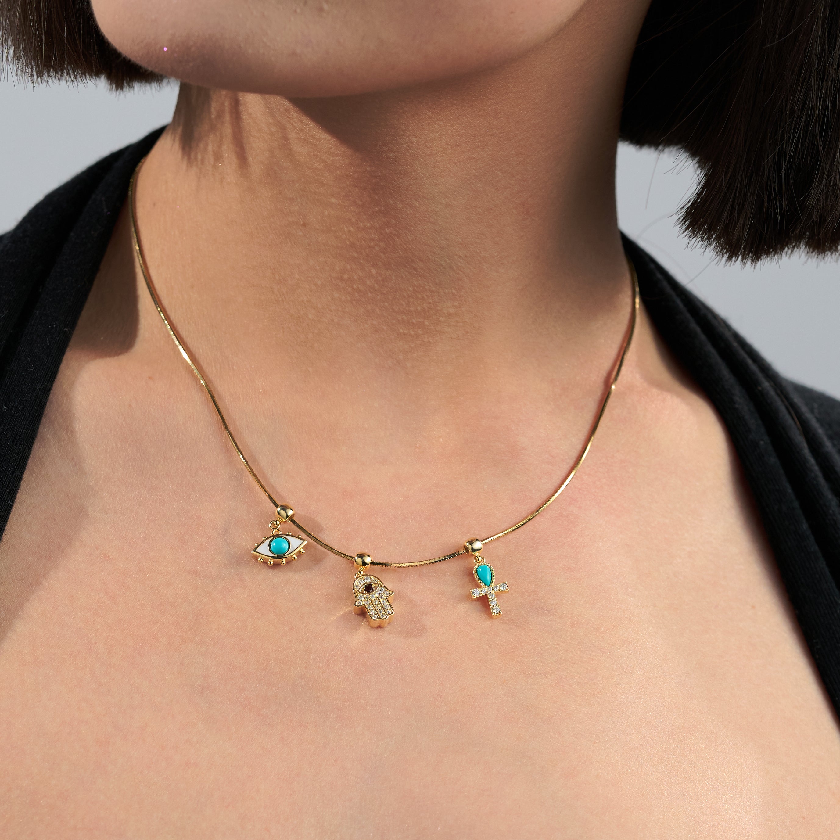 Woman wearing a gold-plated necklace with blue eye, hamsa, and ankh pendants