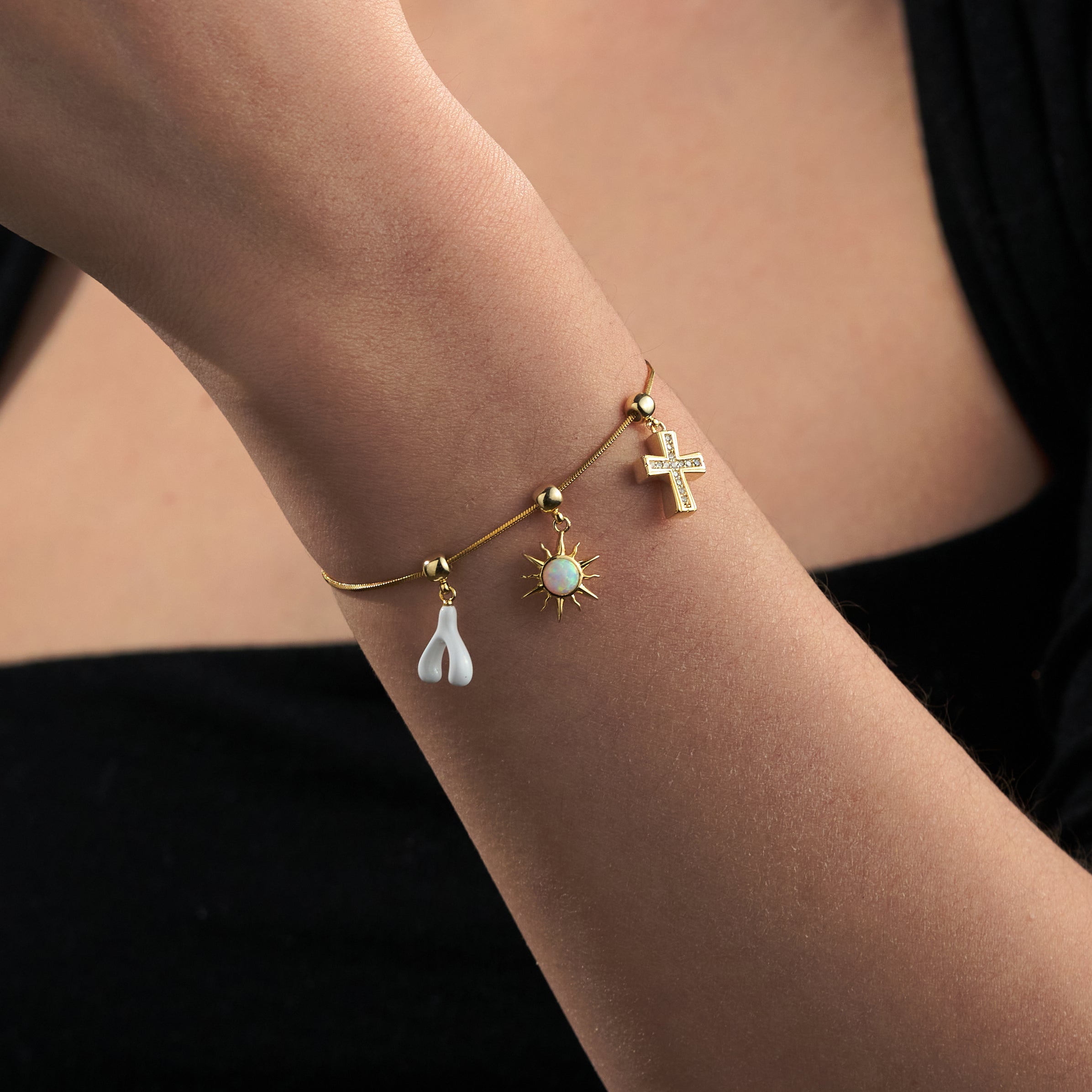 Gold bracelet with cross, sun, and pearl charms on woman's wrist