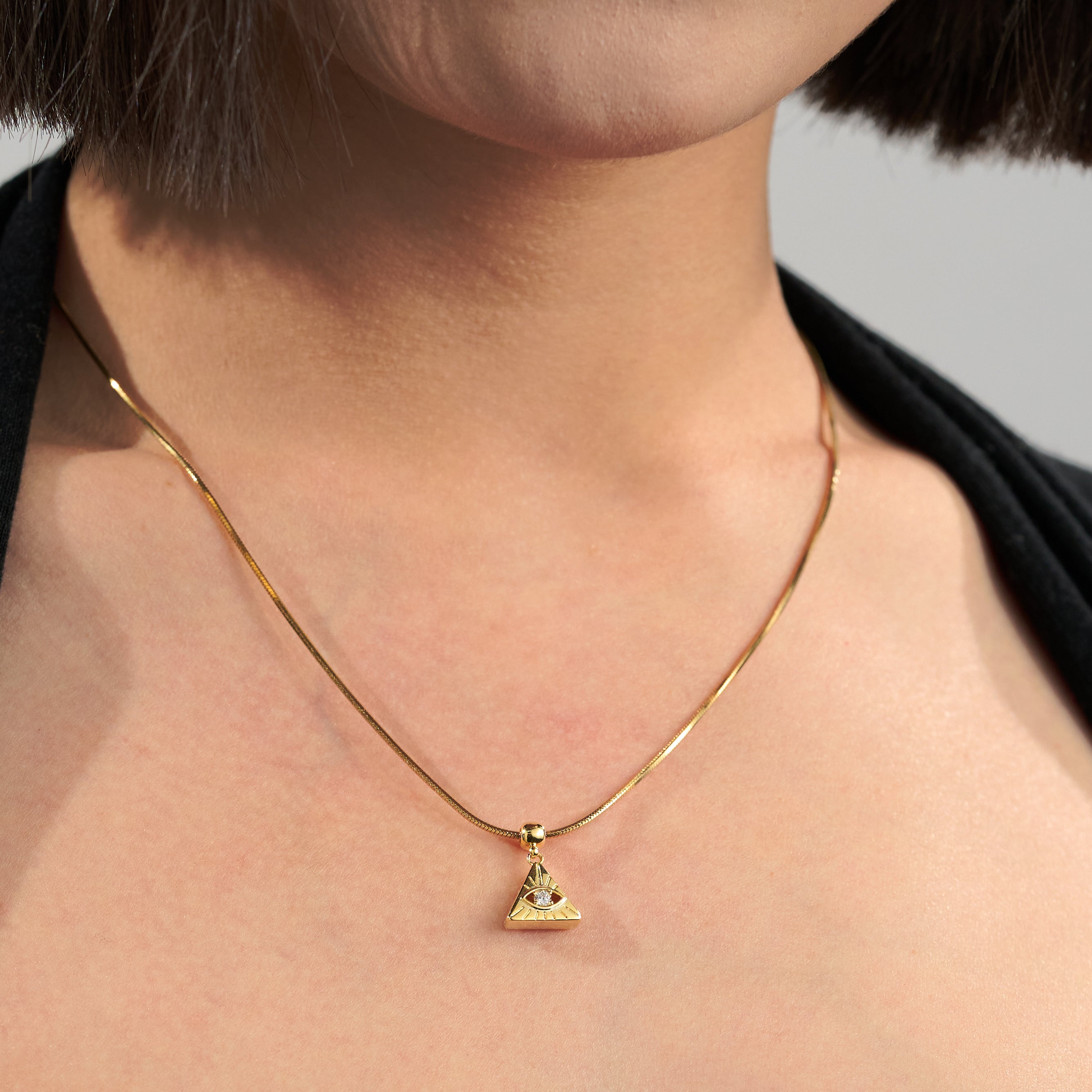 Gold-plated triangle eye pendant necklace on woman's neck, minimalist jewelry