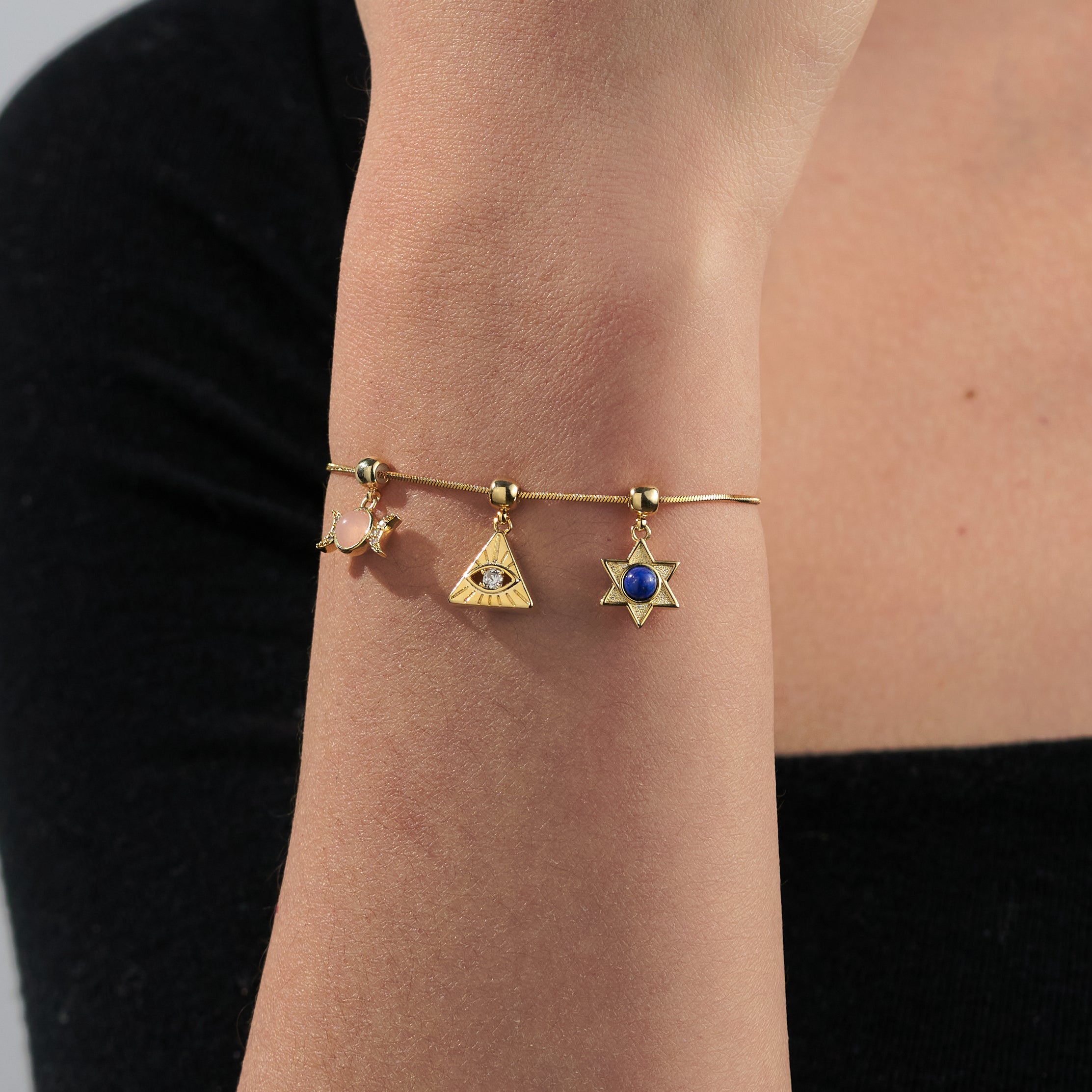 Gold-plated charm bracelet with triangle, star, and moon pendants on a woman's wrist