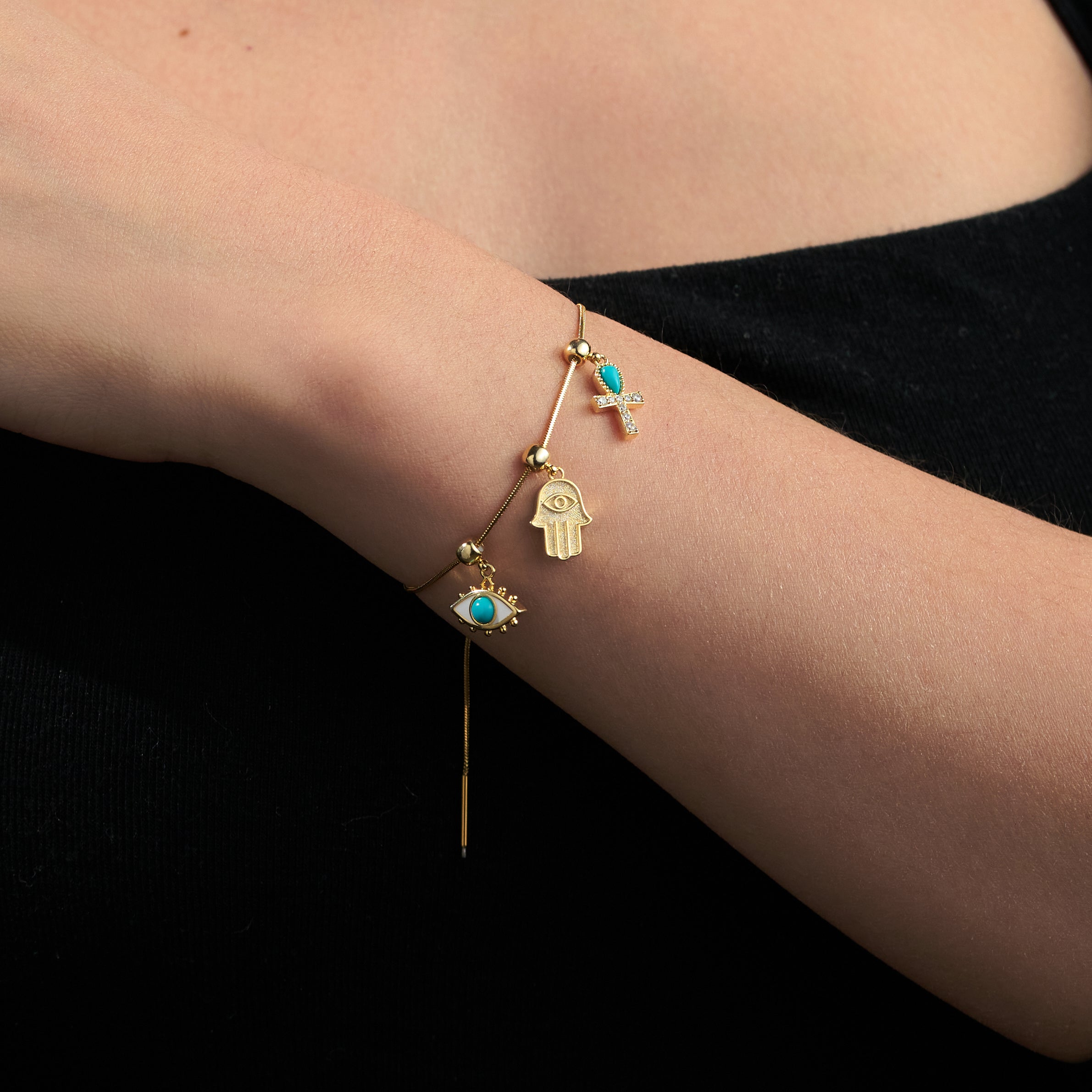 Gold-plated charm bracelet with turquoise stones and symbolic pendants on a woman's wrist