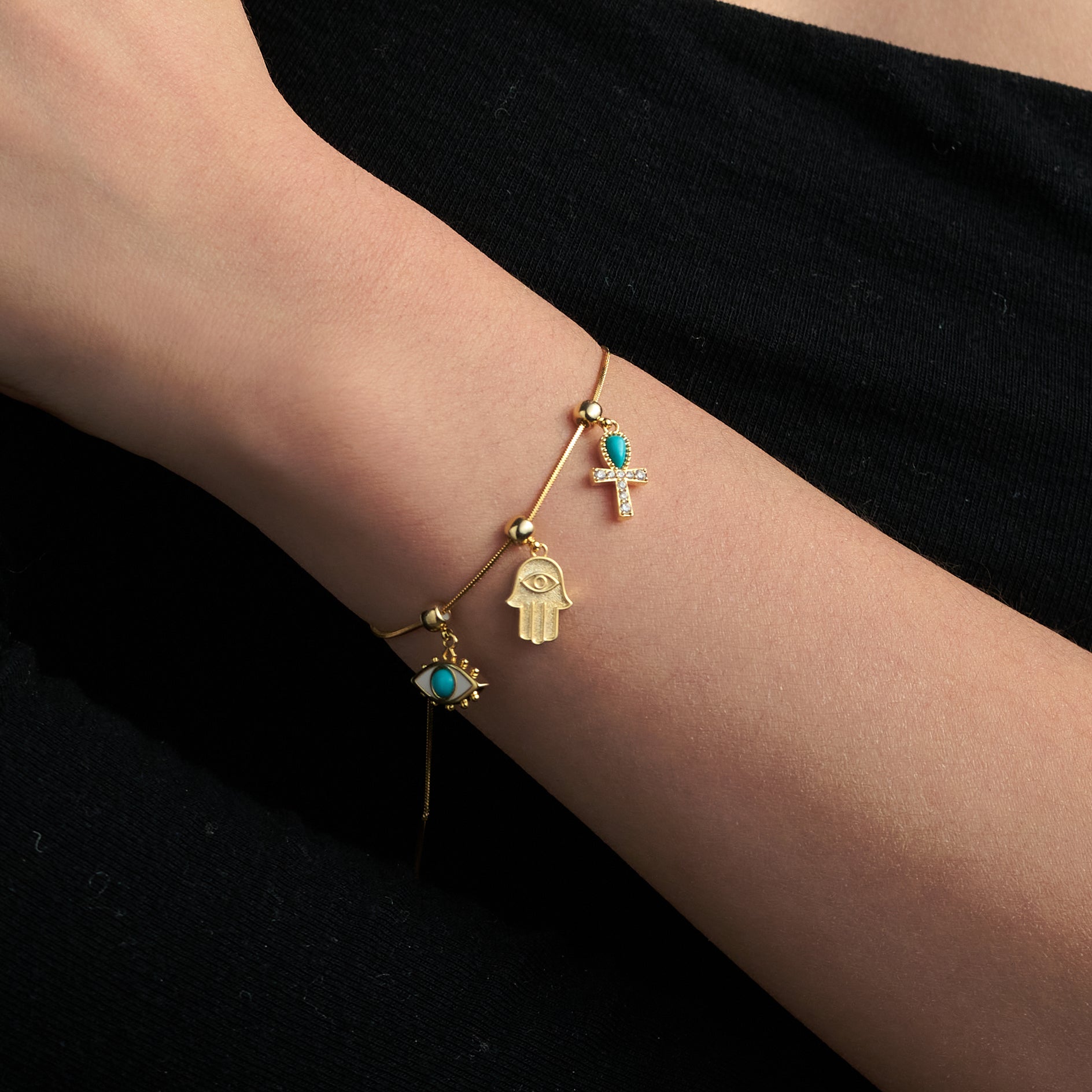 Gold-plated charm bracelet with turquoise accents and symbolic pendants on a woman's wrist