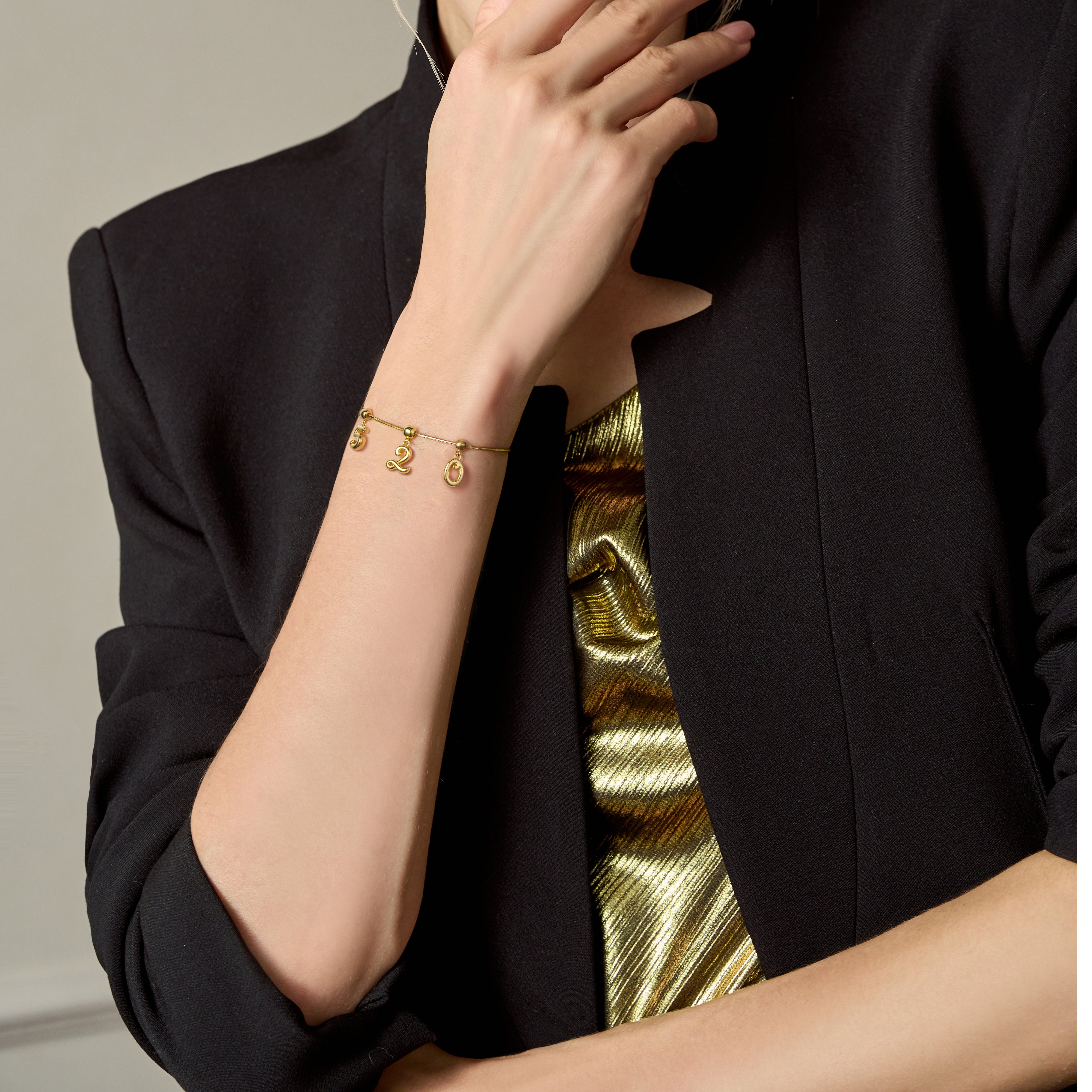 Woman wearing gold-plated number charm bracelet and a gold top under a black blazer