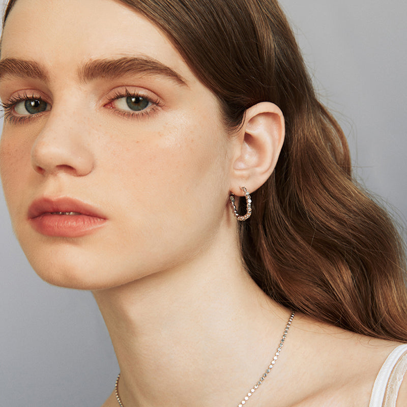 Woman wearing silver chain hoop earrings and a delicate necklace, close-up portrait