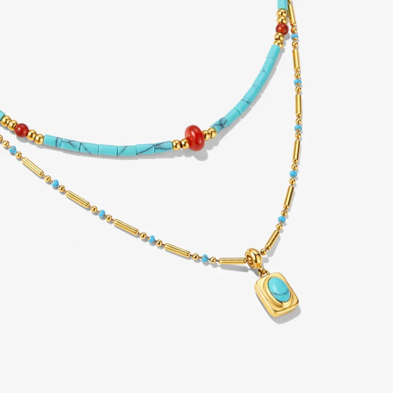 Layered gold-plated necklaces with turquoise and coral beads, pendant detail, on white background