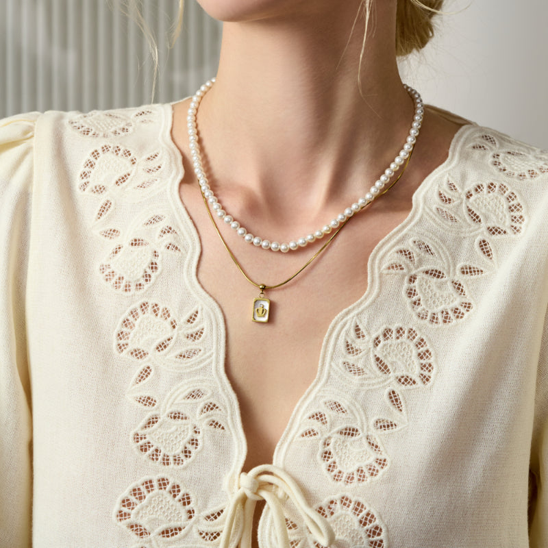 Woman wearing layered gold-plated pendant necklace and pearl necklace with lace cream blouse