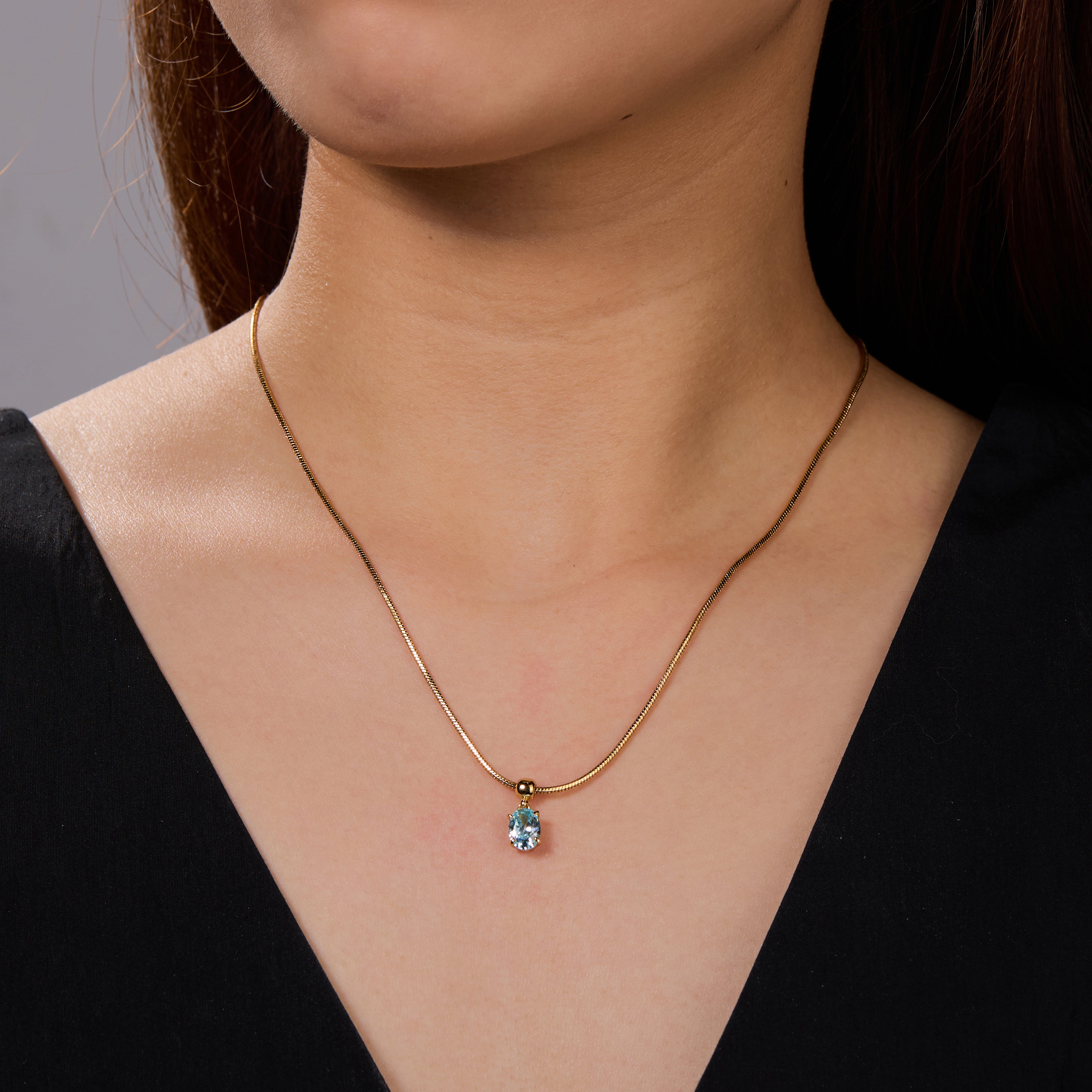 Gold-plated necklace with blue gemstone pendant on woman wearing black top