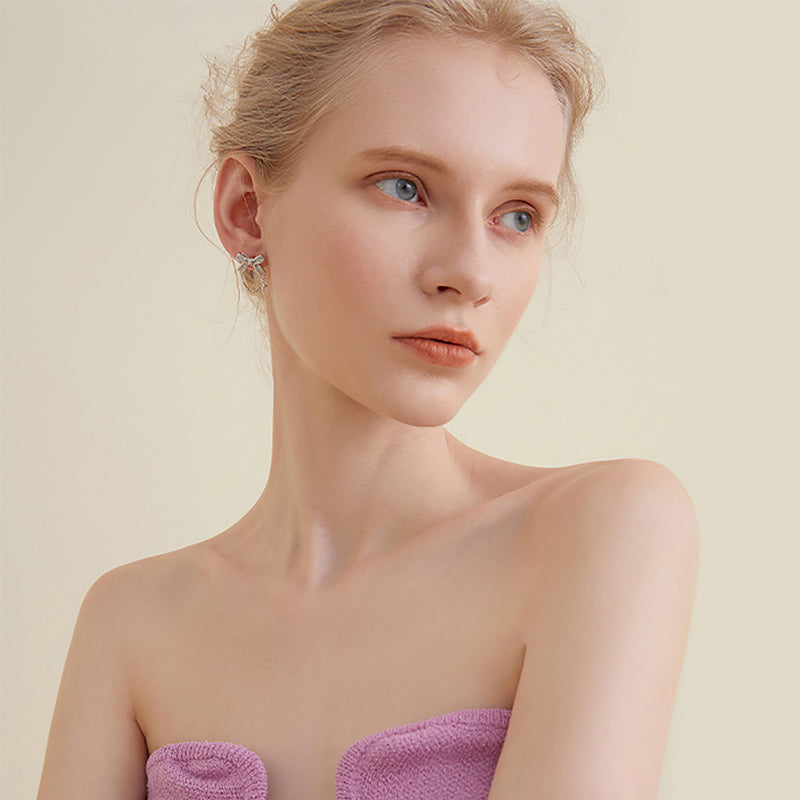 Woman wearing statement gold-plated earrings and a lilac strapless top against a beige background