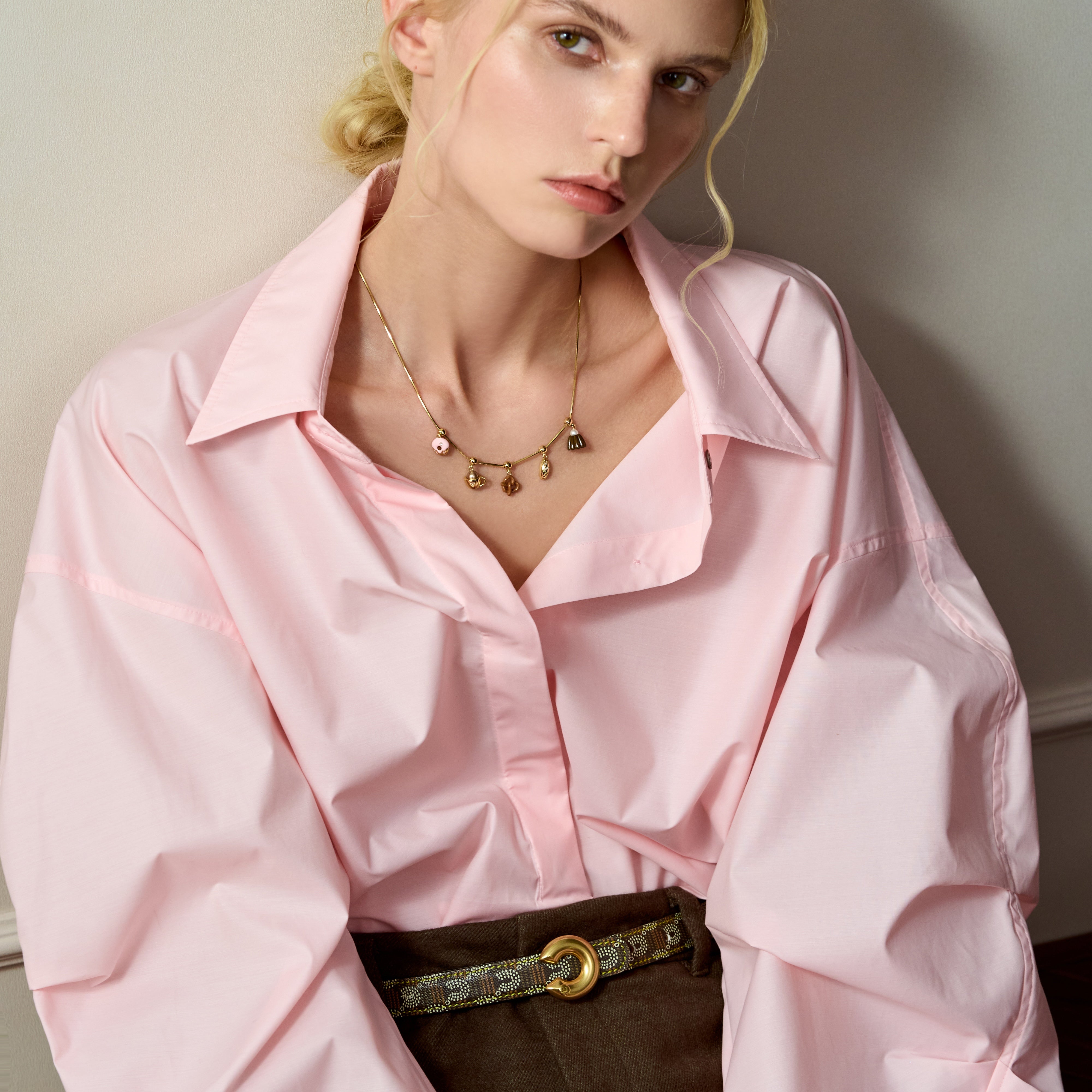 Woman in pink blouse wearing gold-plated charm necklace and elegant belt