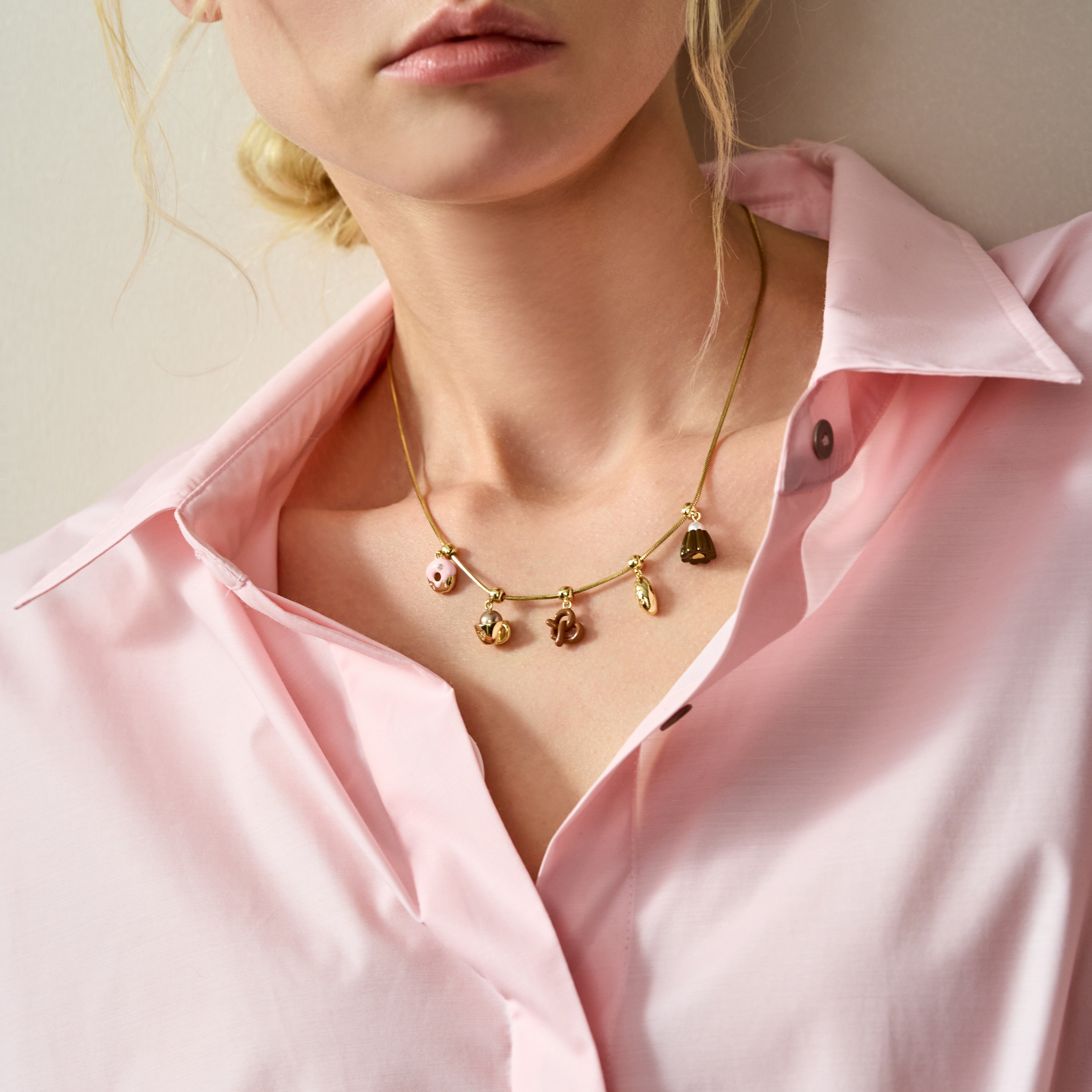 Woman wearing gold-plated charm necklace with pink shirt, elegant jewelry style
