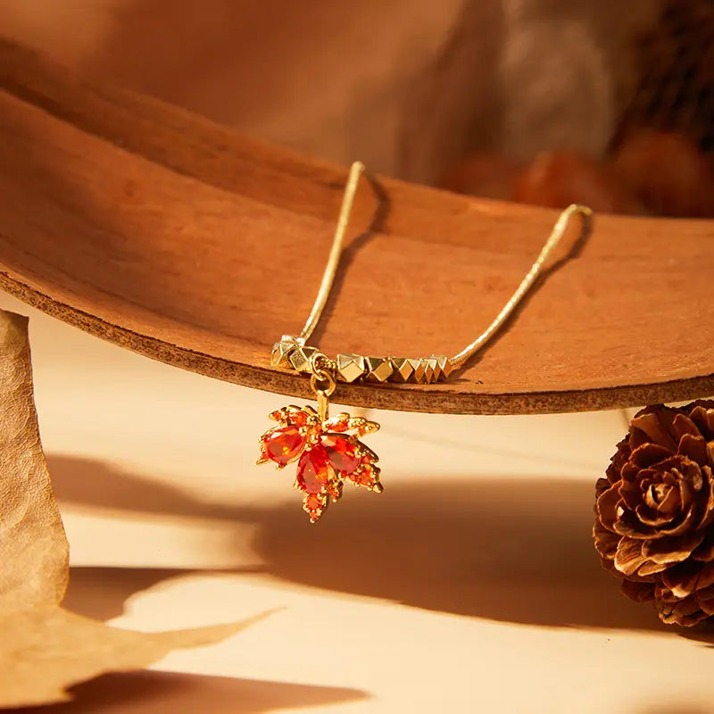 Gold-plated necklace with red leaf pendant displayed on rustic background