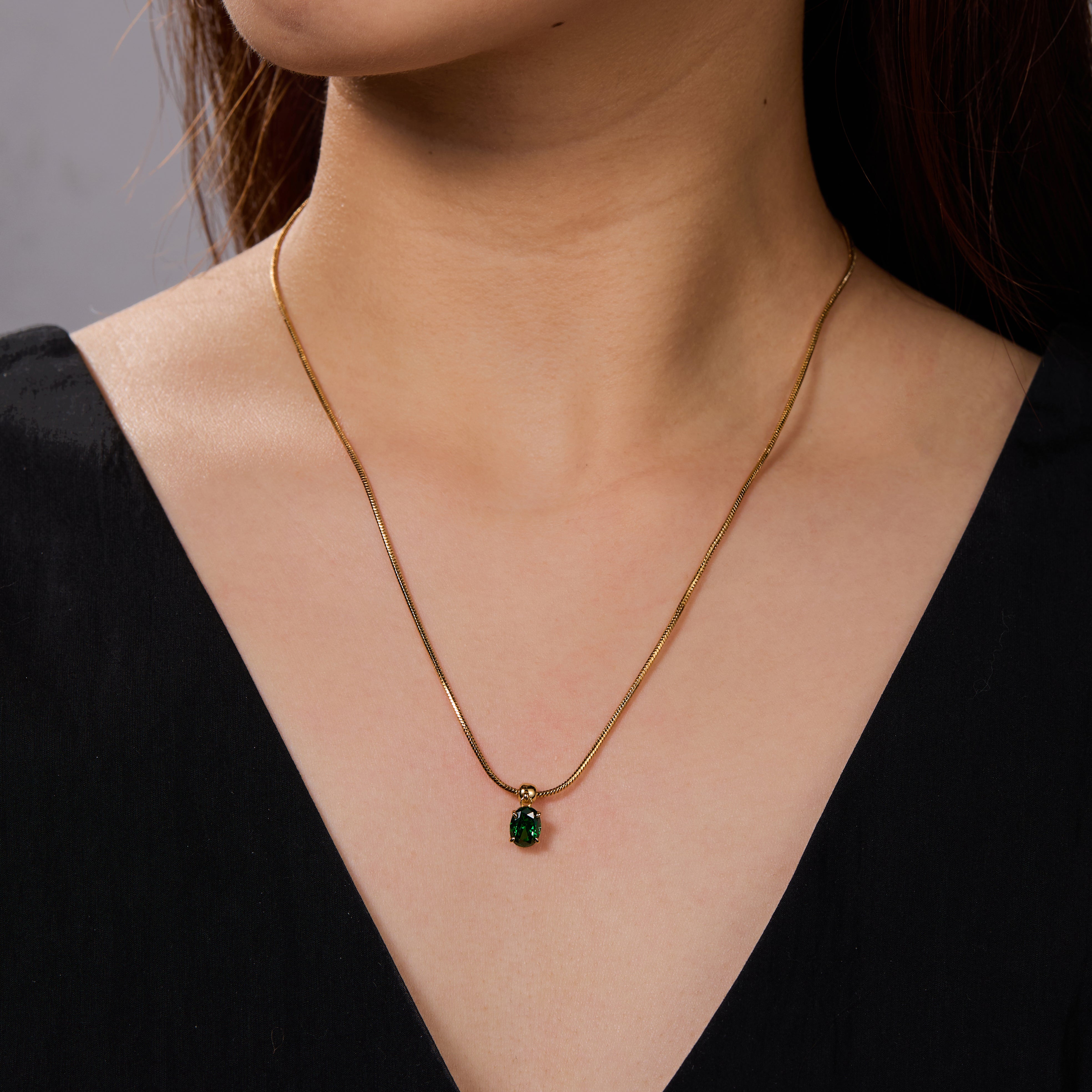 Gold-plated necklace with green gemstone pendant on woman in black V-neck top