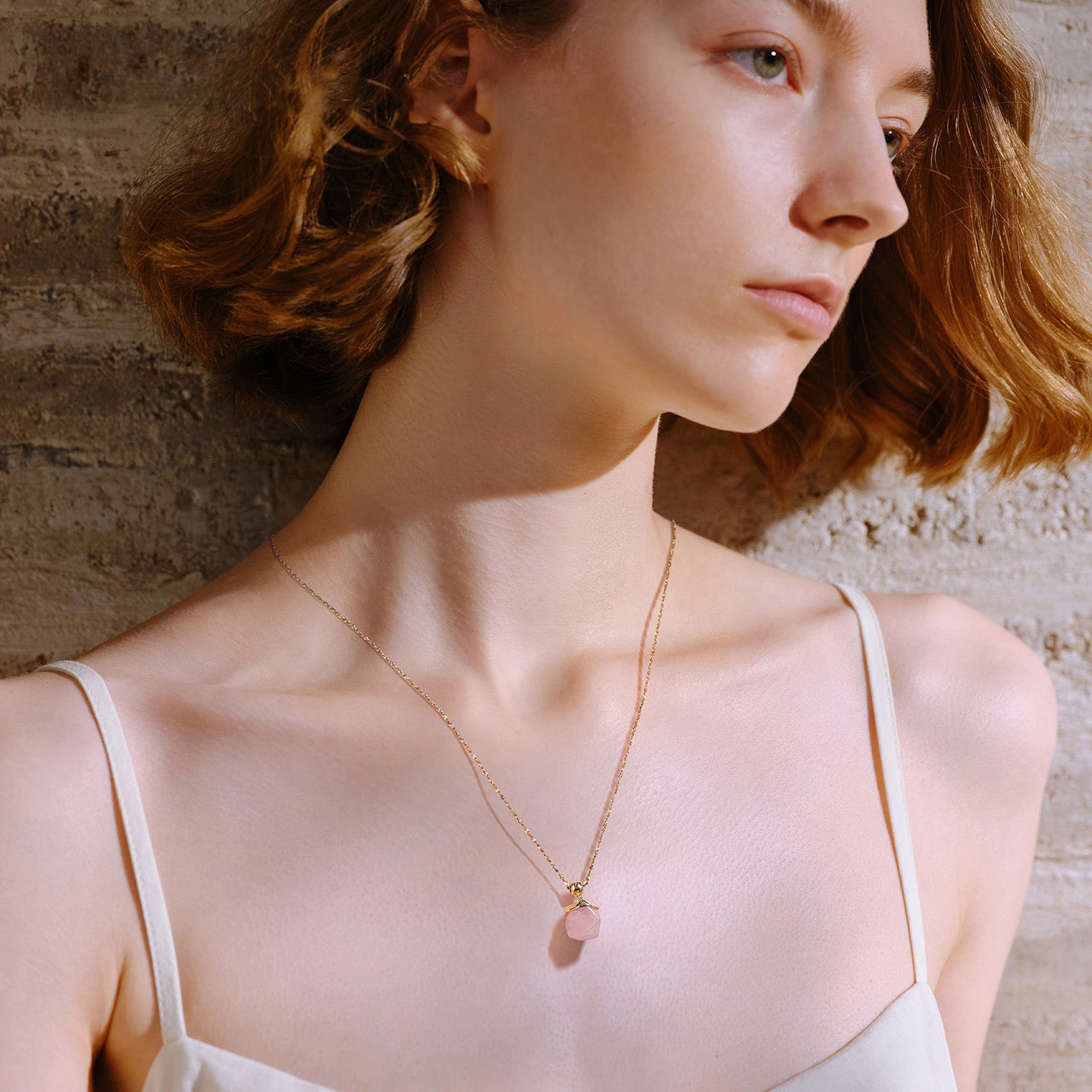 Woman wearing gold-plated necklace with pink pendant, minimalist elegant jewelry