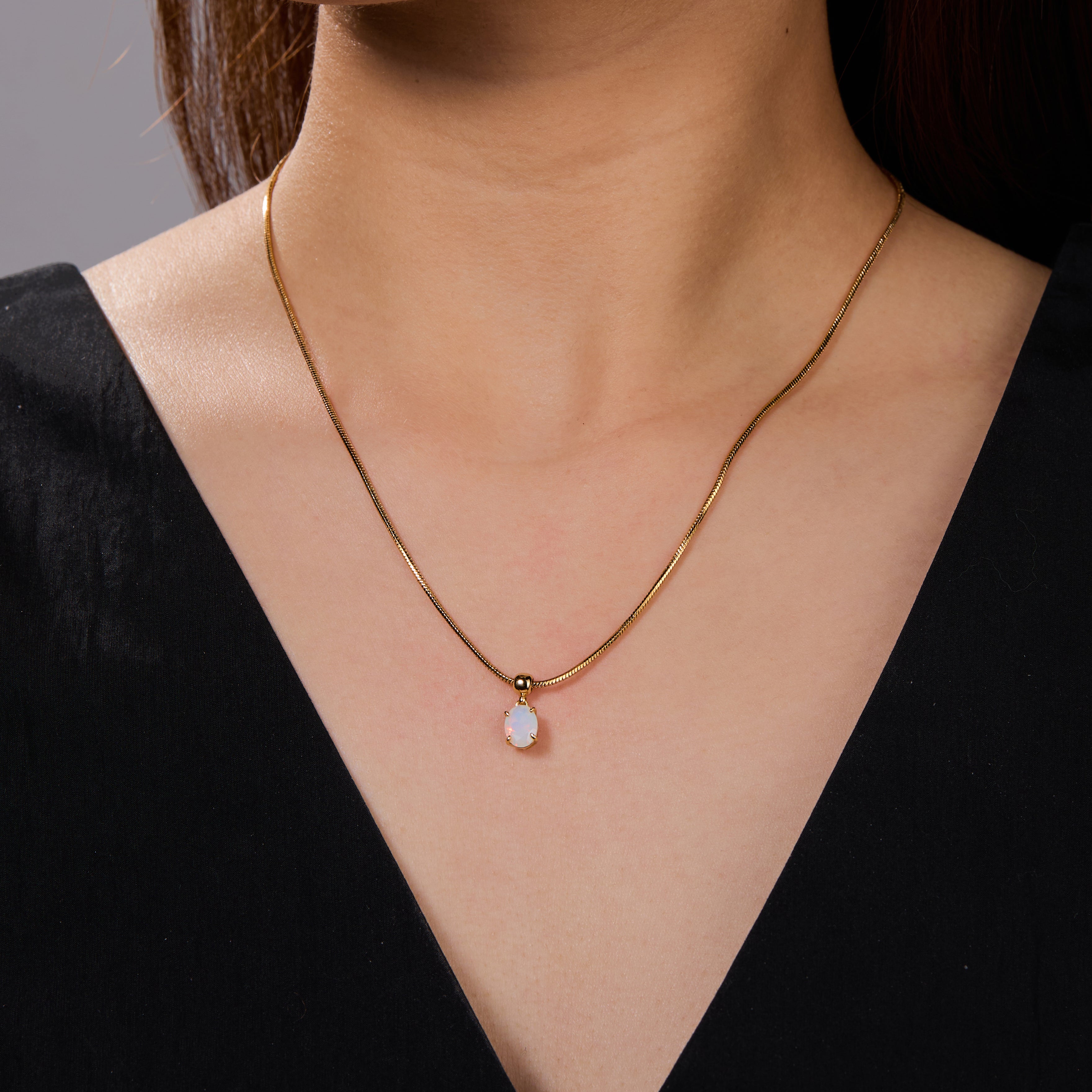 Gold-plated necklace with single opal pendant on woman wearing black V-neck top