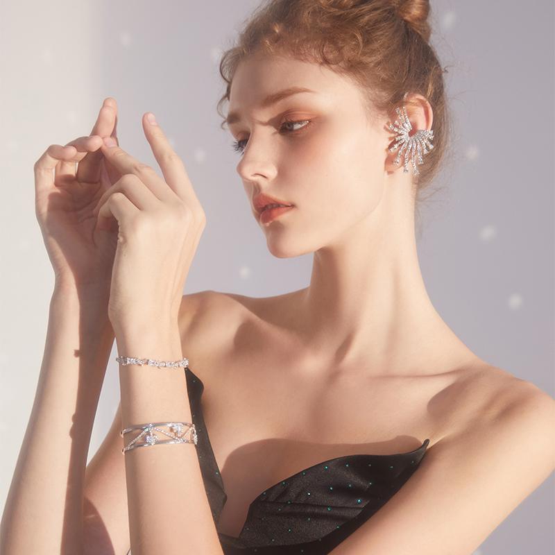 Woman wearing elegant statement crystal ear cuff and silver bracelets, dressed in black