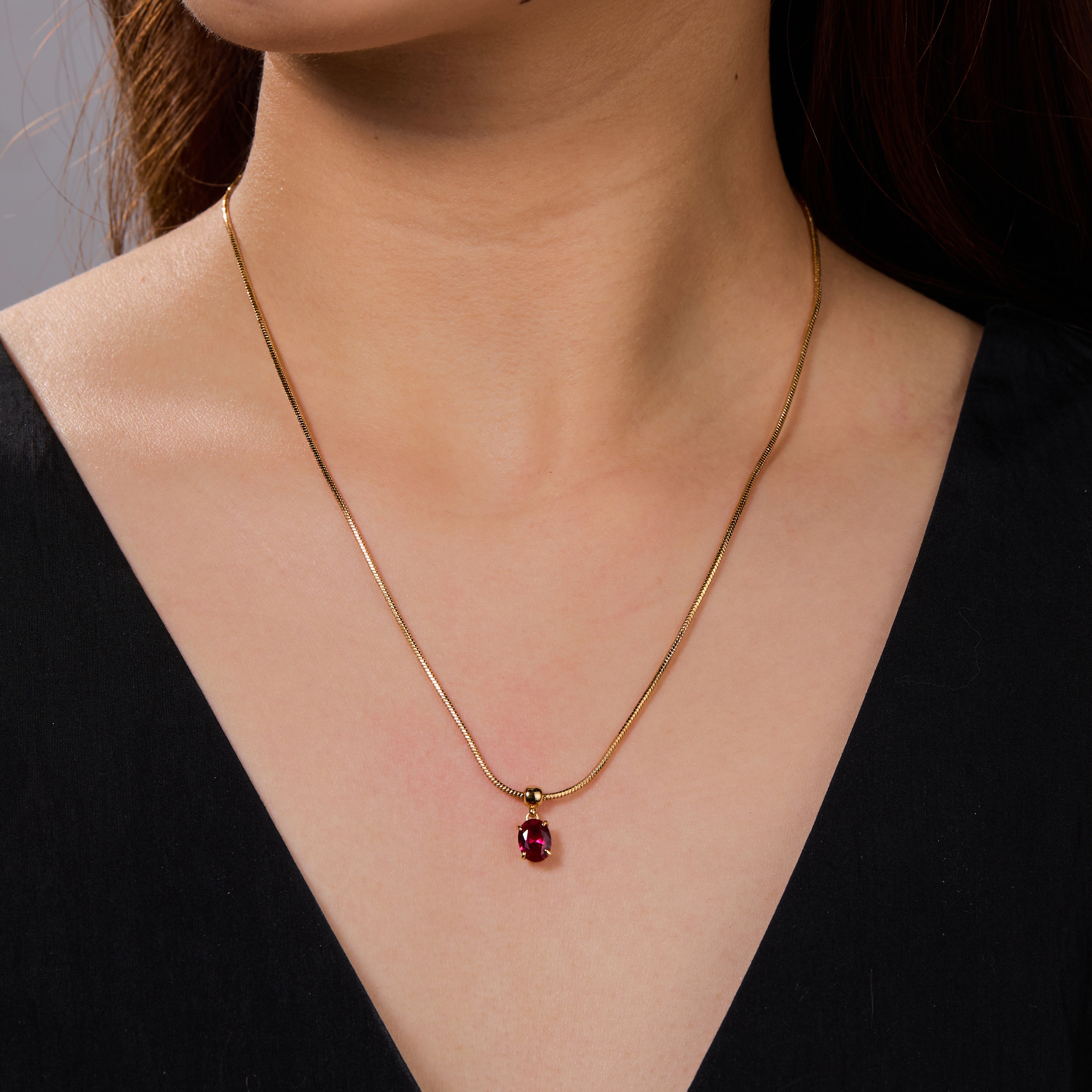 Gold-plated necklace with red gemstone pendant on woman in black V-neck top