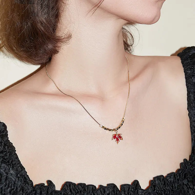 Gold-plated necklace with red leaf pendant worn with a black textured dress