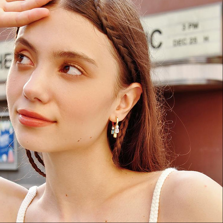 Woman wearing gold-plated statement earrings with colorful stones, braided hair, outdoor setting